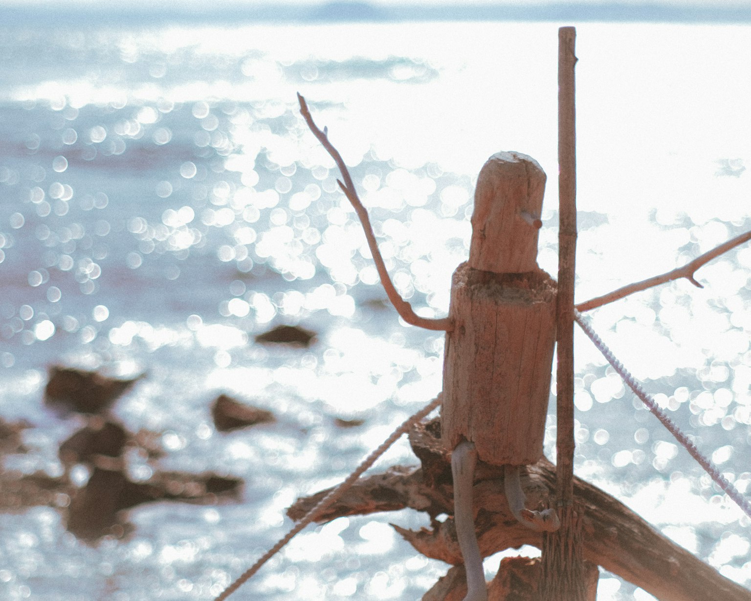 Eine Holzskulptur steht am Meer mit funkelndem Wasser im Hintergrund