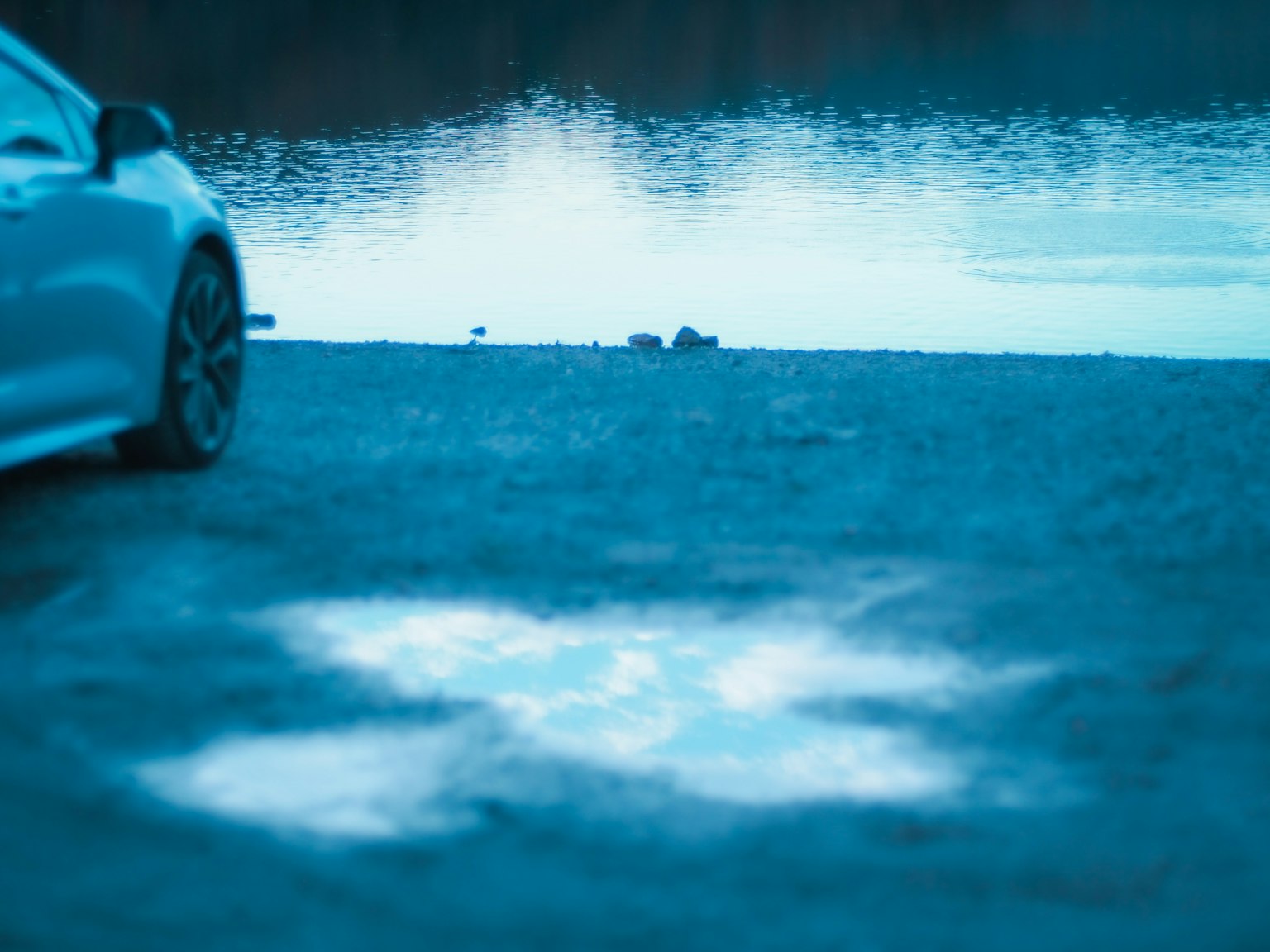 Un'auto parcheggiata vicino a un lago tranquillo con riflessi sulla superficie dell'acqua