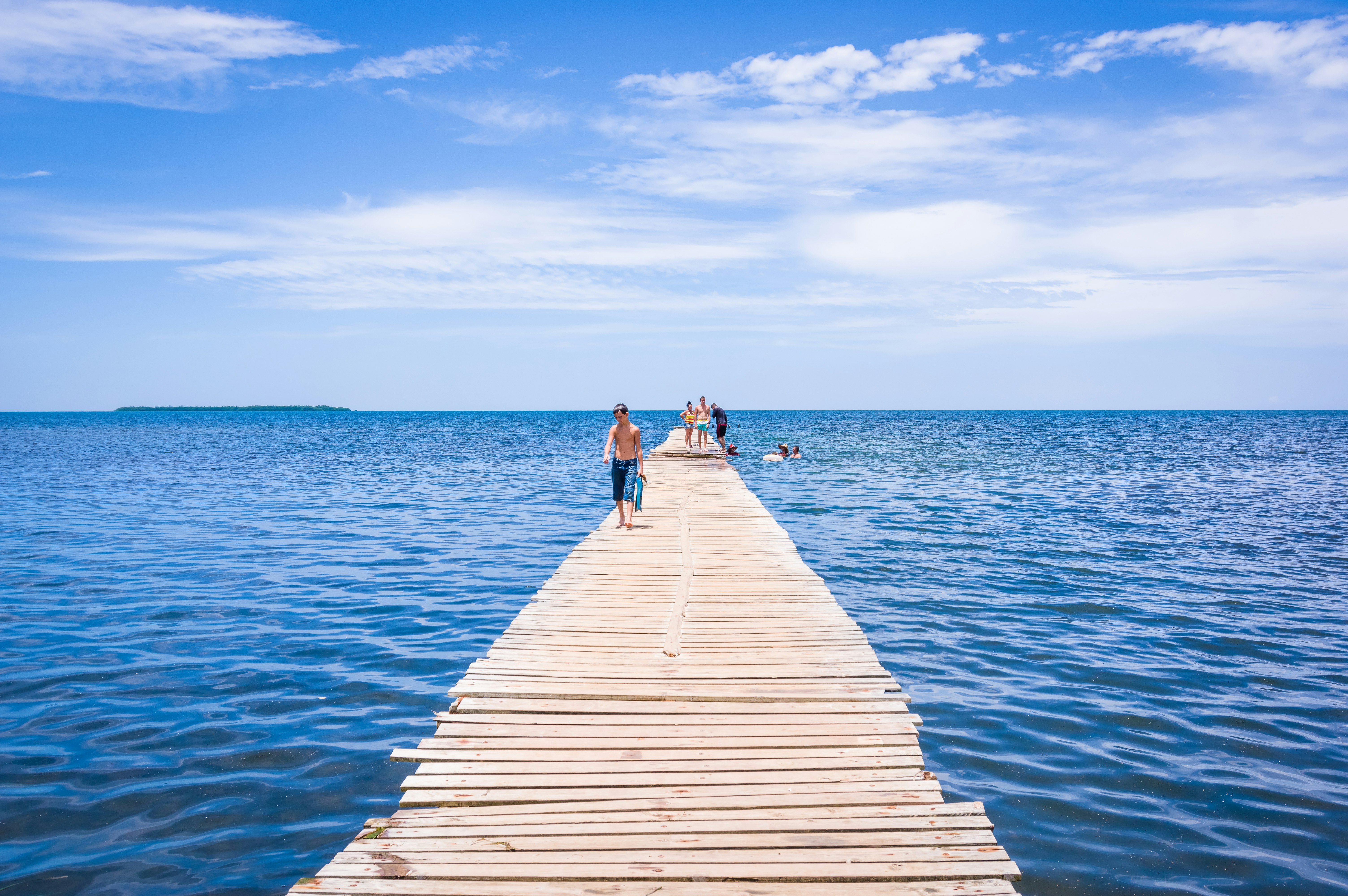blue ocean scene with people walking along a wooden pier