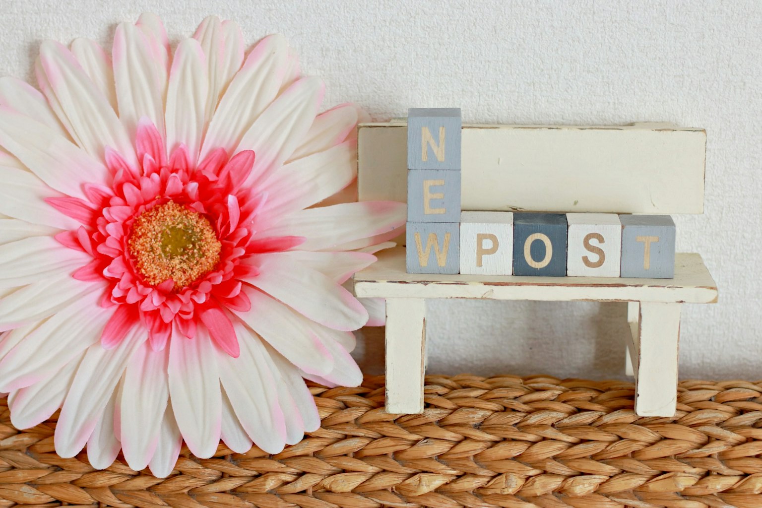 Un banco blanco con letras de bloques que dicen 'NEW POST' y una gran flor rosa