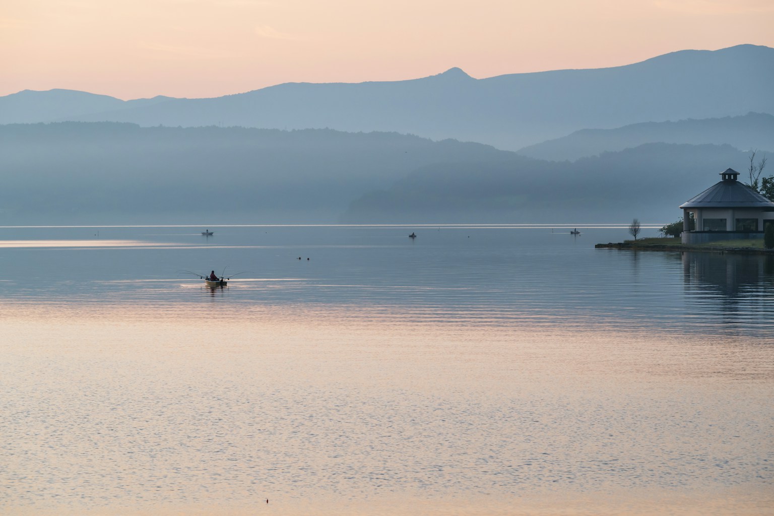 Danau yang tenang dengan perahu sendirian dan pegunungan jauh saat matahari terbit