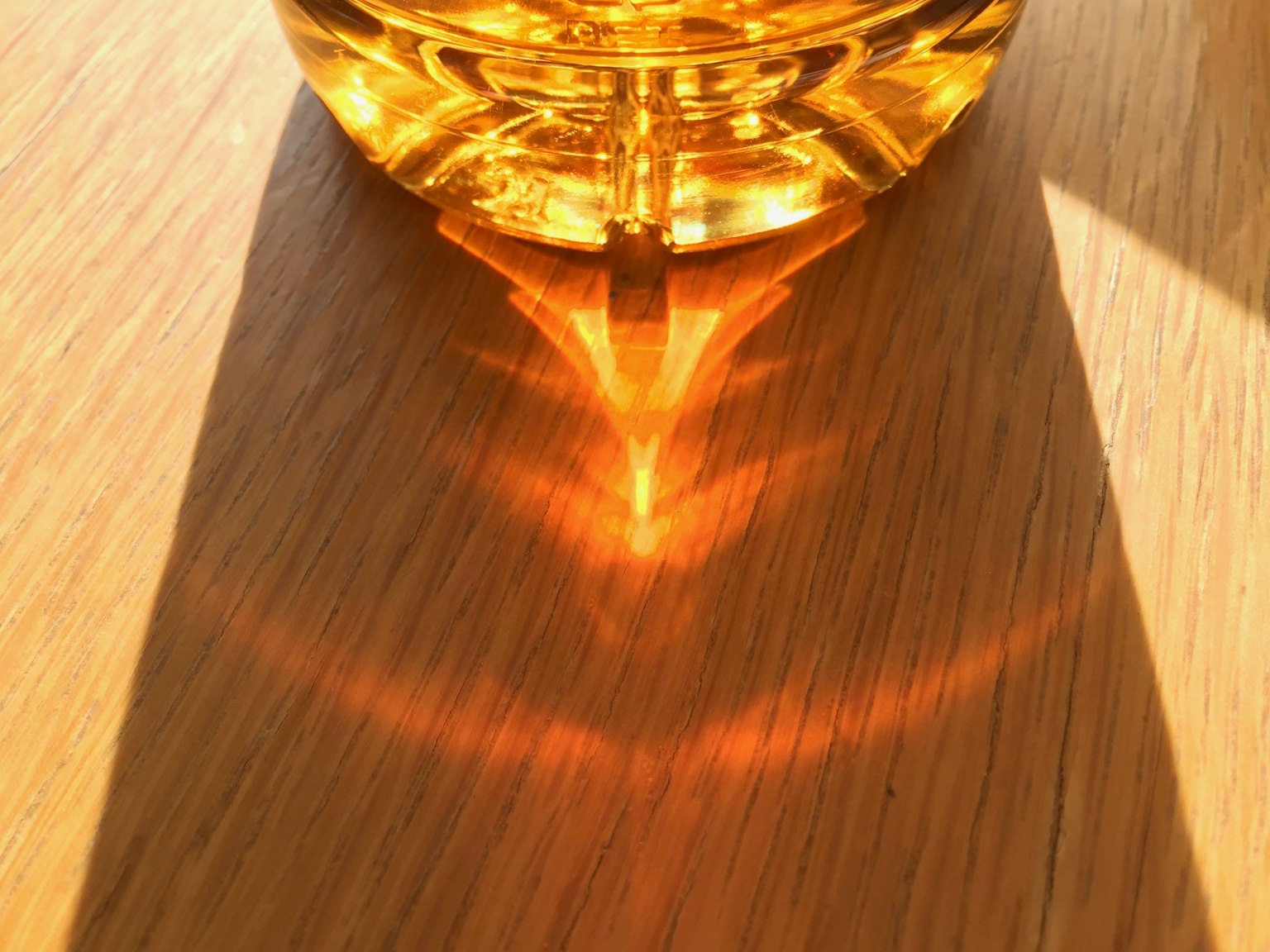 Riflessione di luce arancione da una bottiglia trasparente su un tavolo di legno