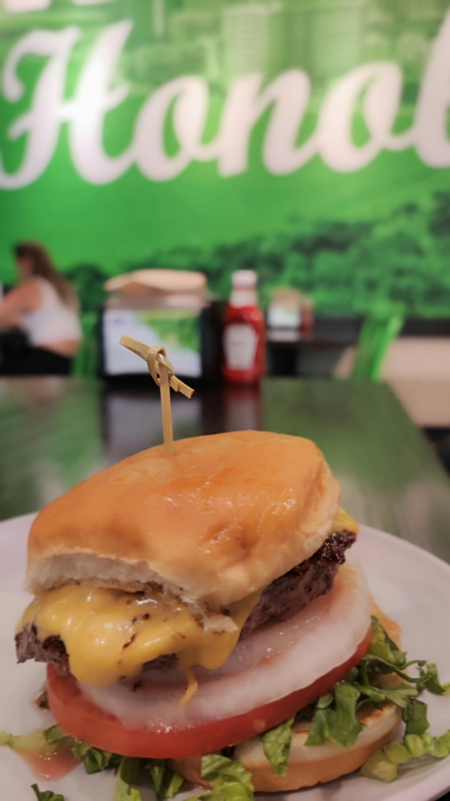 Cheeseburger con queso derretido y verduras frescas en un plato con fondo verde de Honolulu