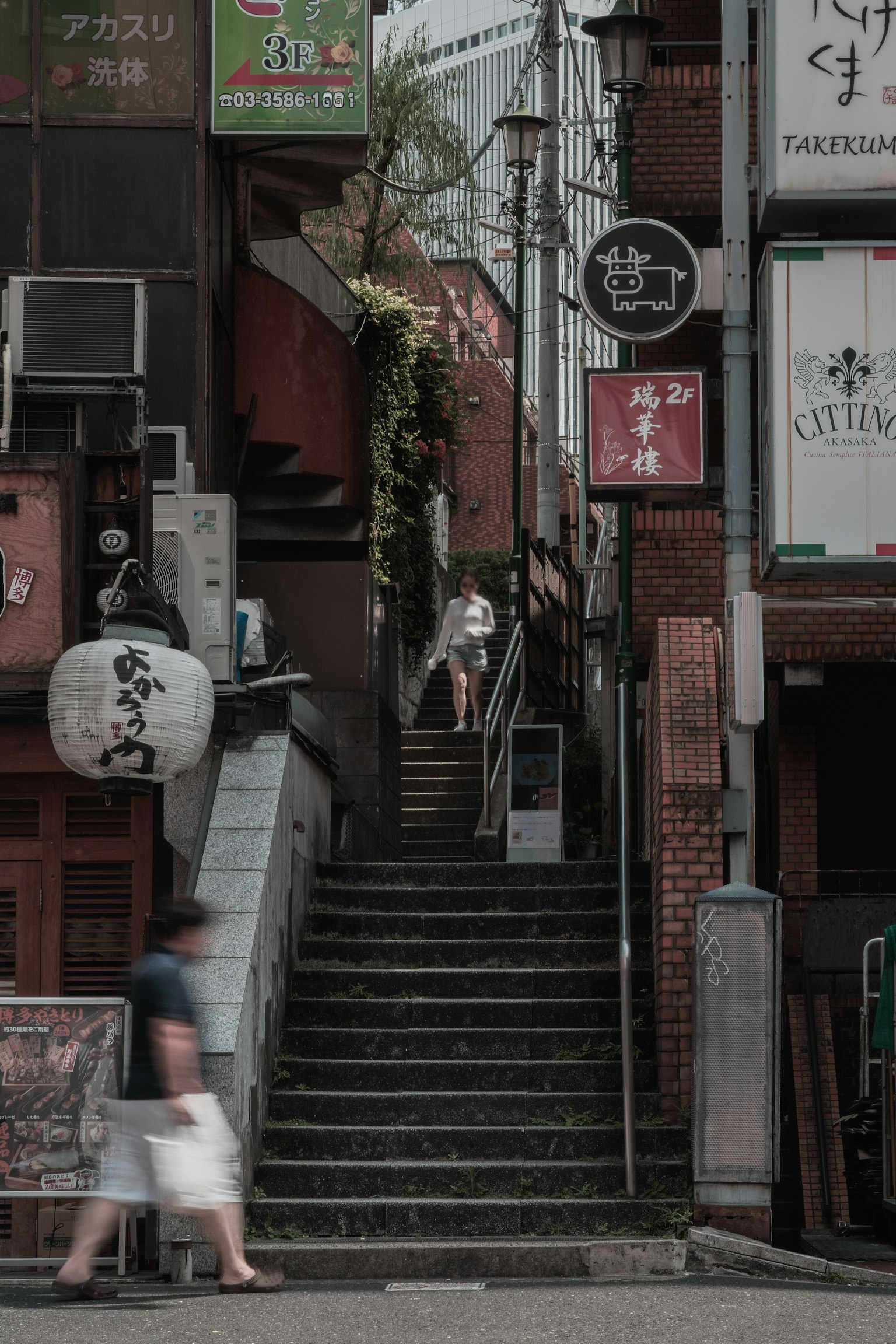 Enge Gasse mit Treppen und verschiedenen Schildern, eine Person läuft