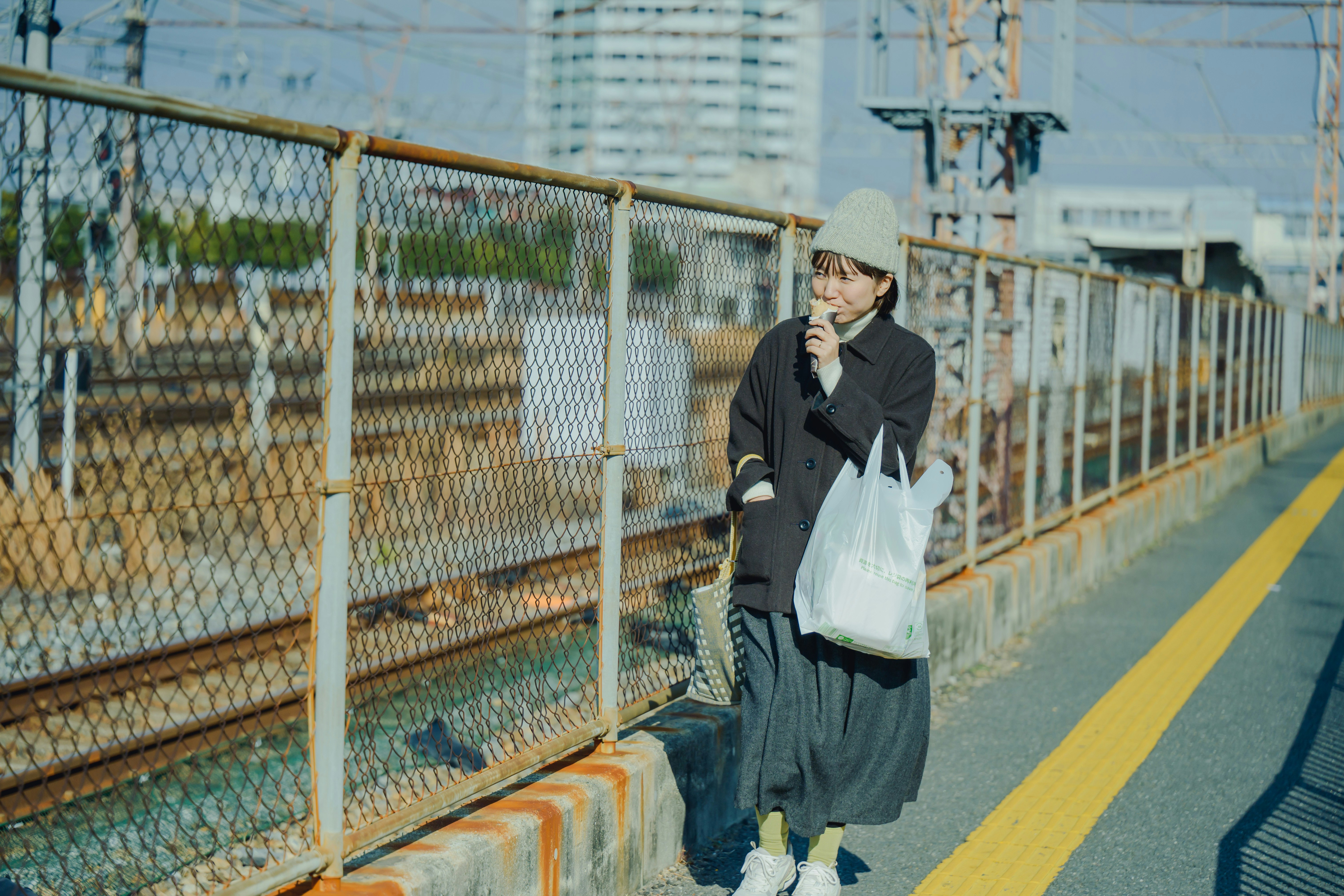 高架のフェンス沿いを歩く買い物袋の女性