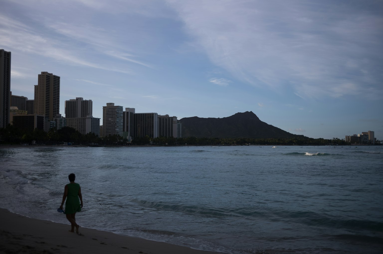 Persona caminando por una playa hawaiana con Diamond Head al fondo