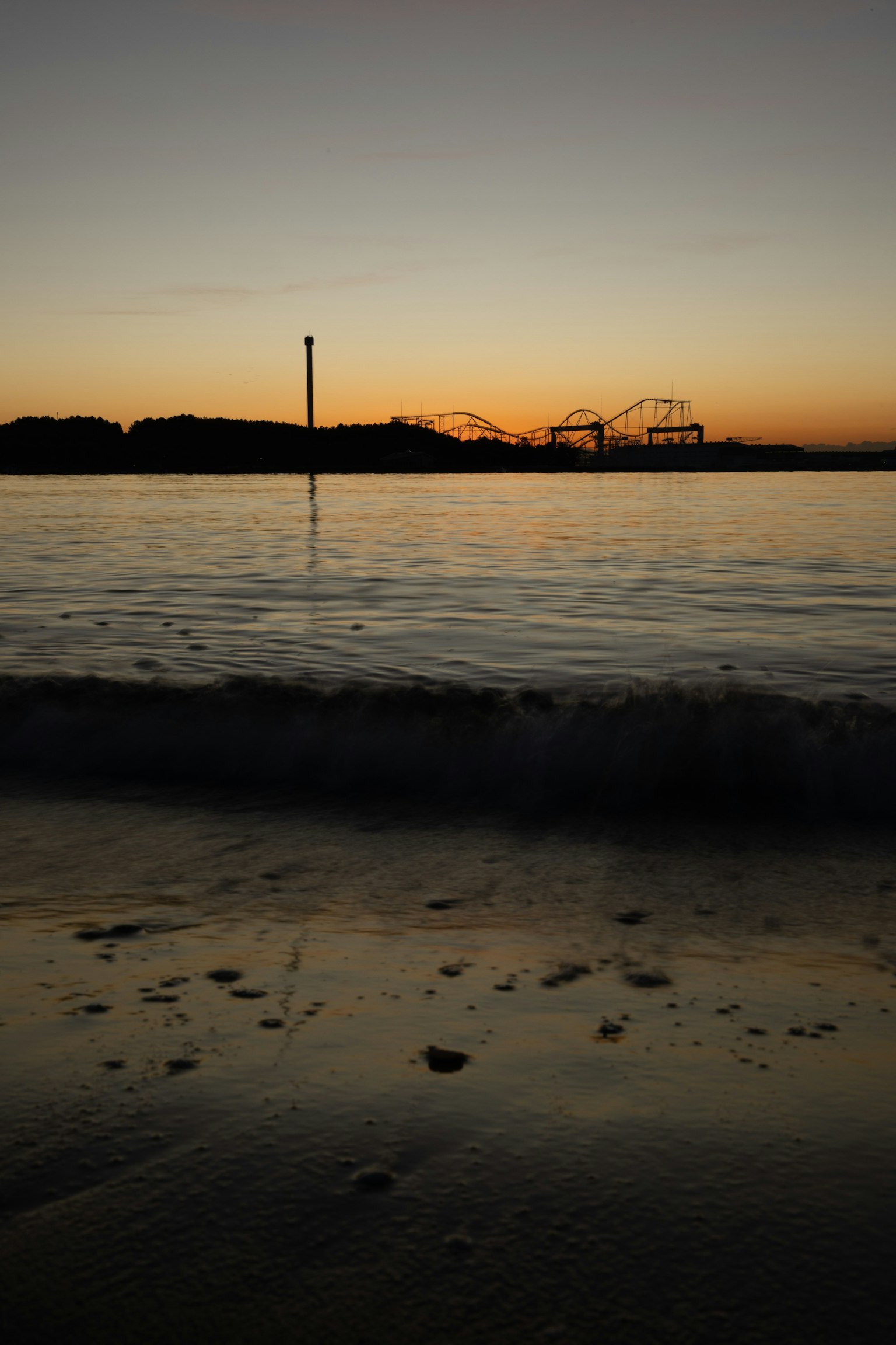 Vue de coucher de soleil sur la côte avec des vagues sur la plage silhouette d'un parc d'attractions au loin