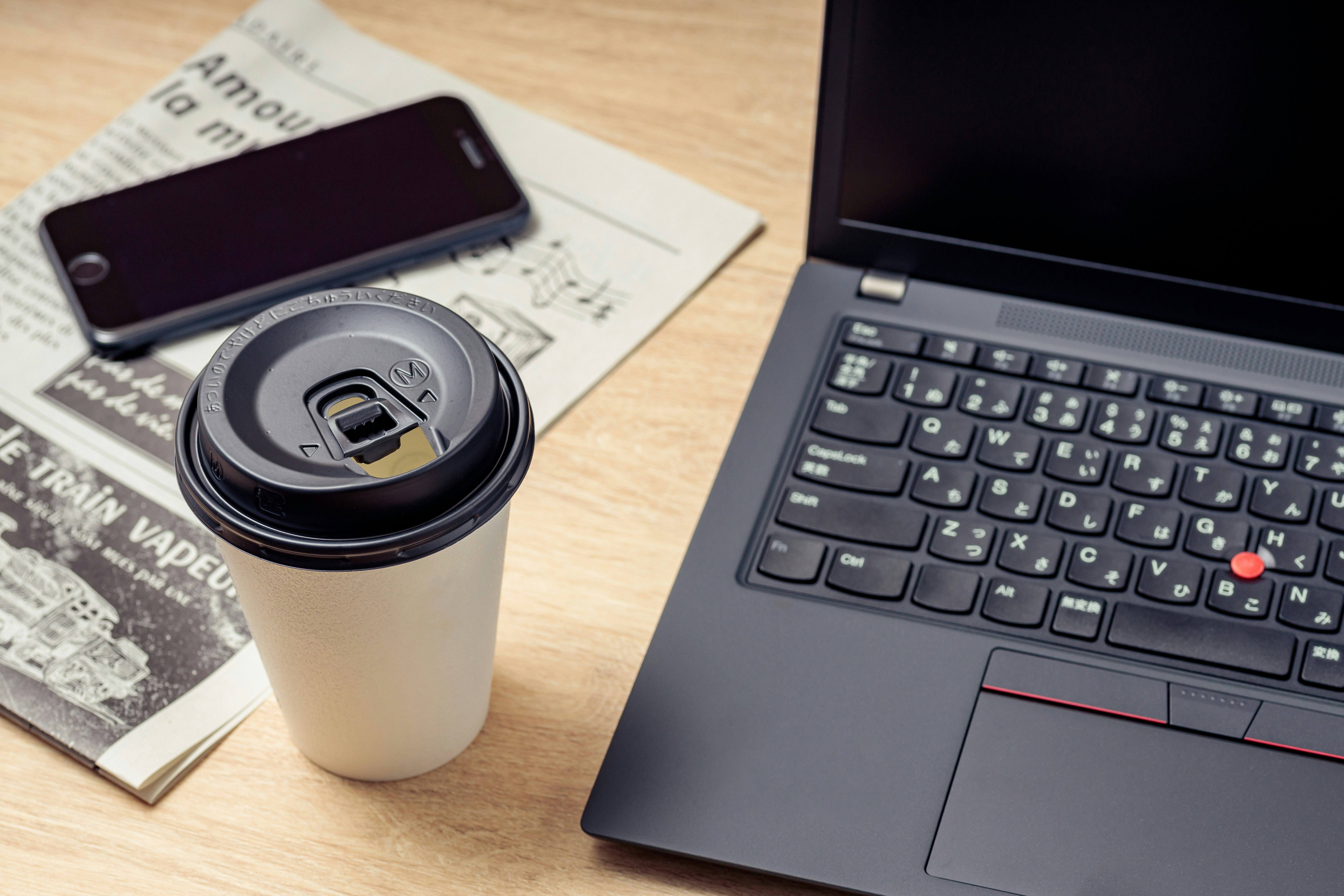 コーヒーと新聞、ノートPCとスマホが並ぶビジネスデスク