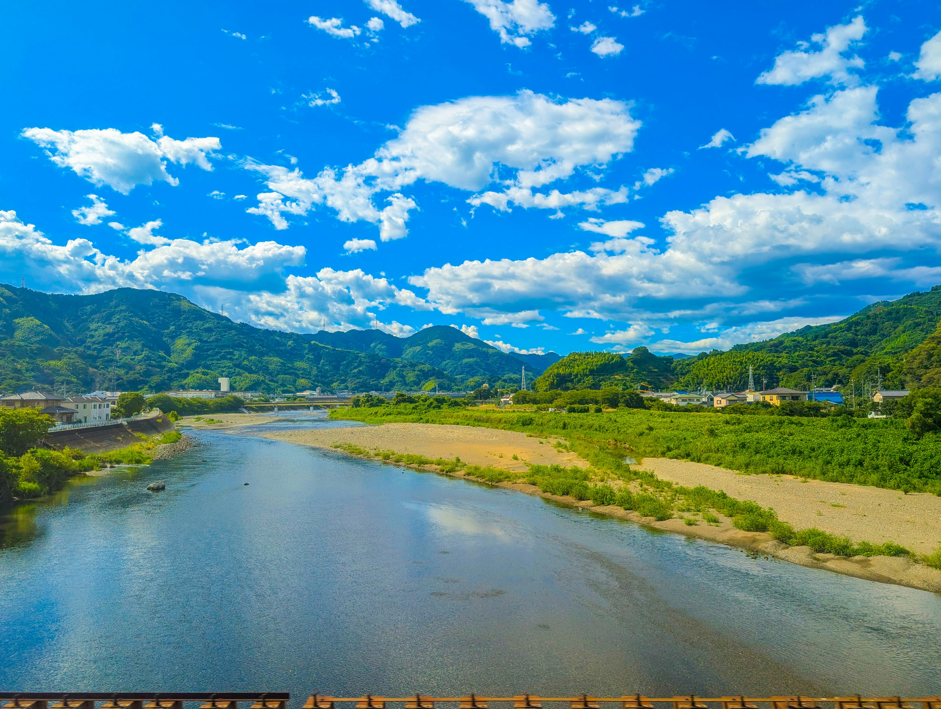 青空と白い雲が広がる美しい風景 川と緑の山々が見える