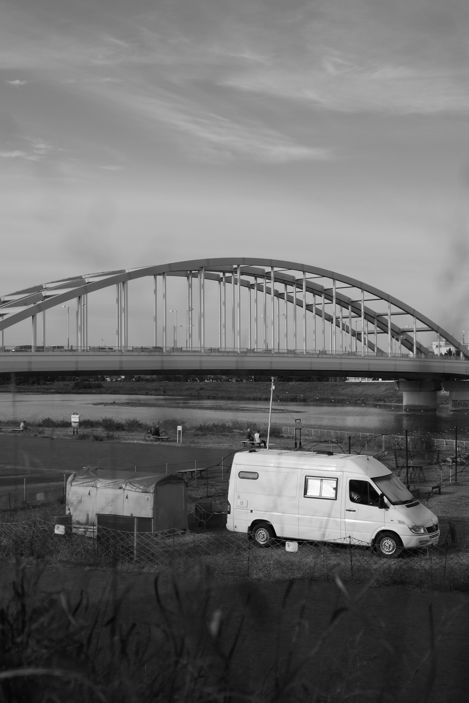 Black and white scene featuring a bridge and a white van