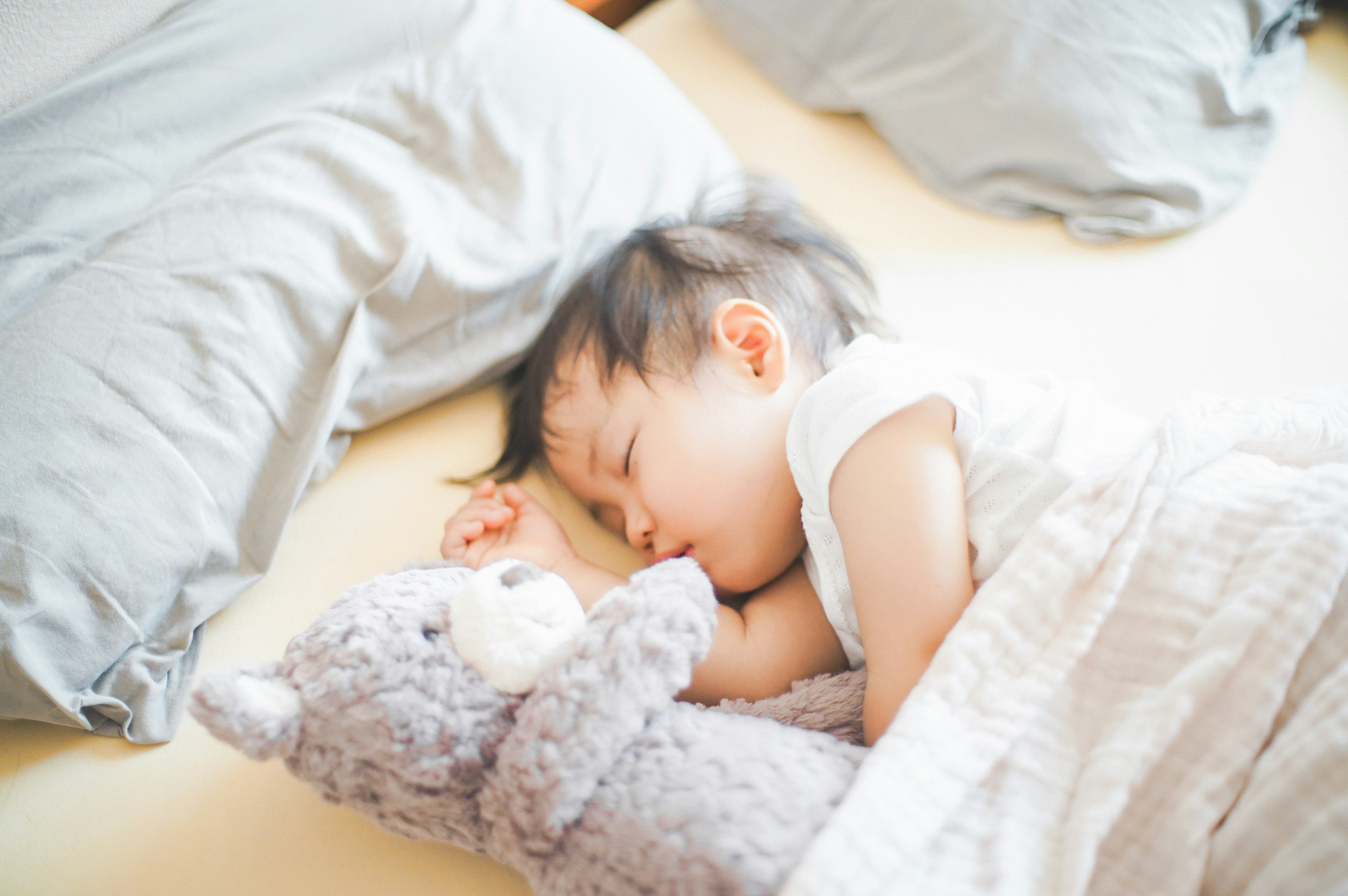 布団の中でぬいぐるみを抱いて眠る赤ちゃん