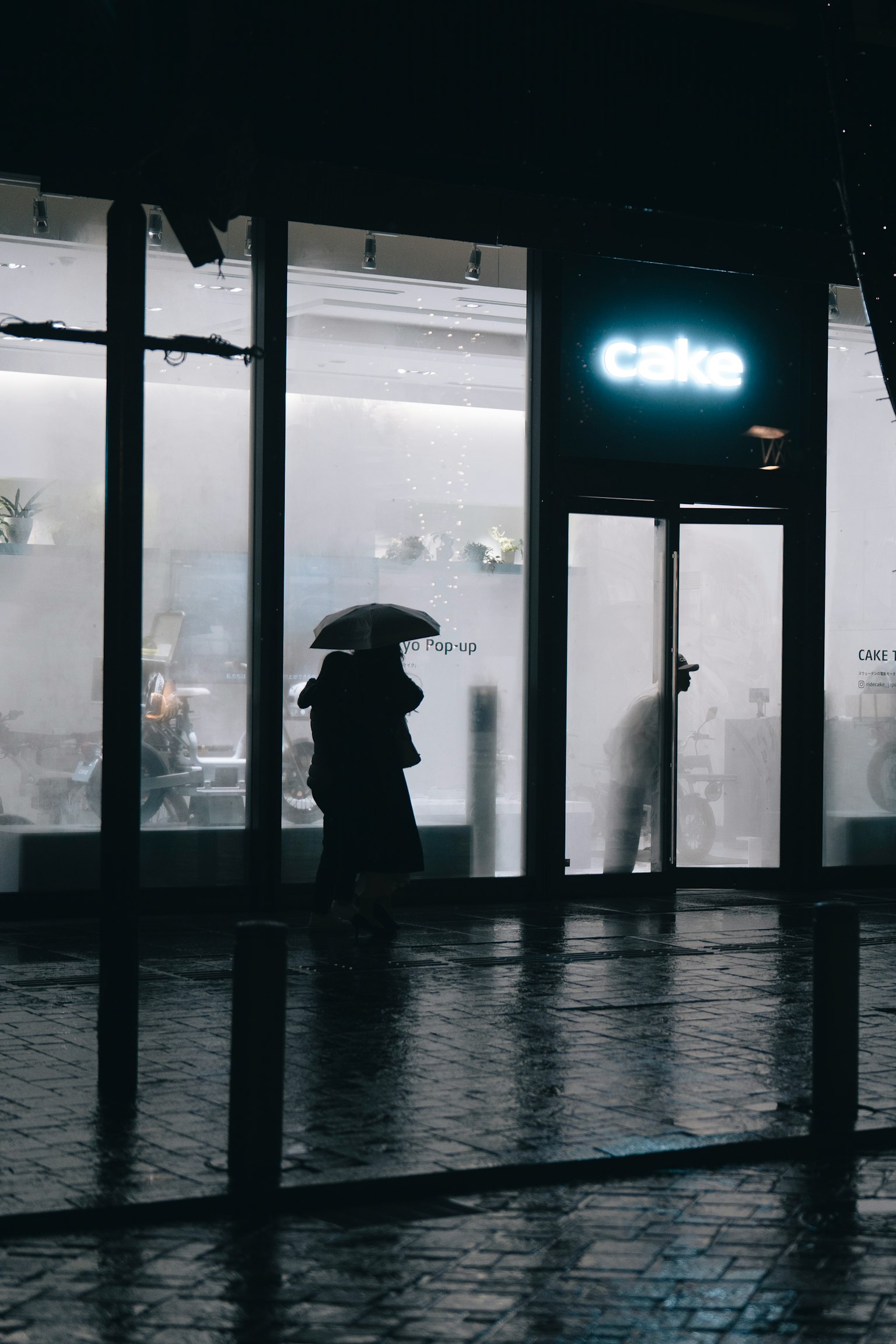 在雨夜中，拿著傘的剪影在咖啡館前