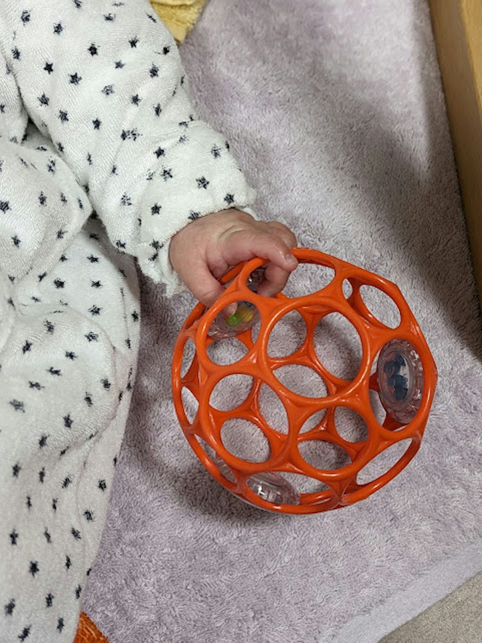 婴儿手握着一个带孔的橙色球