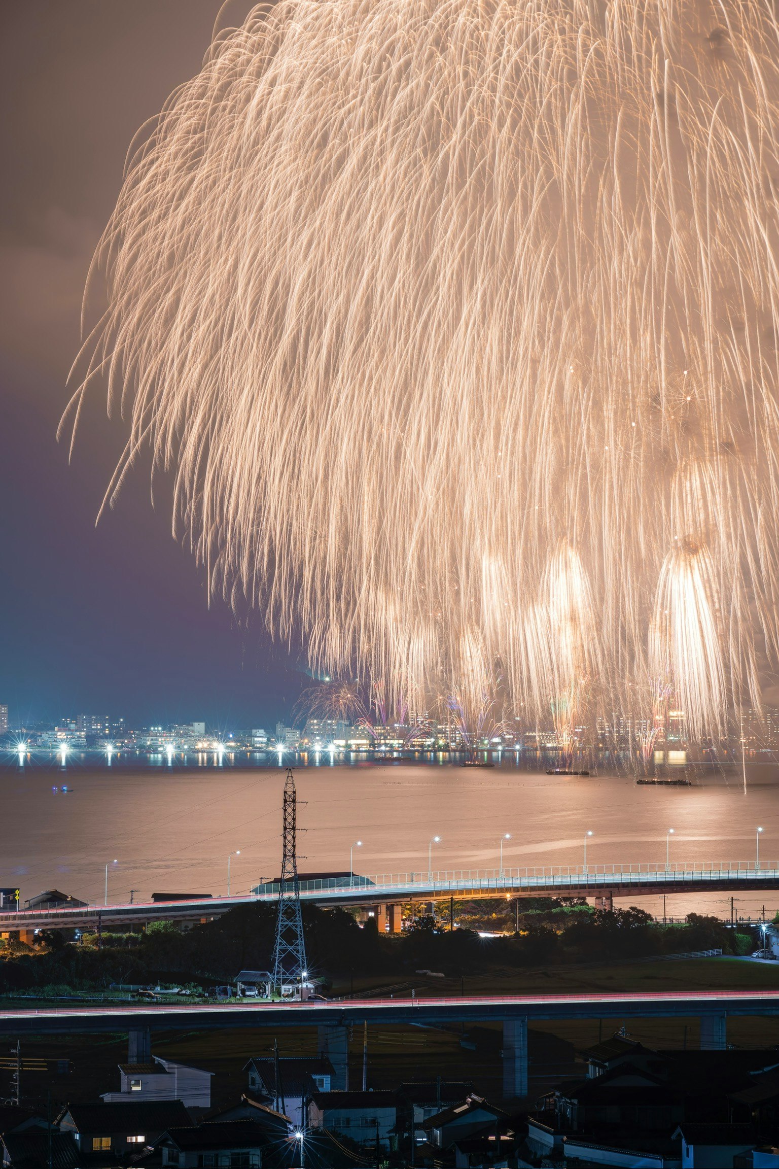 Large fireworks burst in the night sky above a shimmering sea