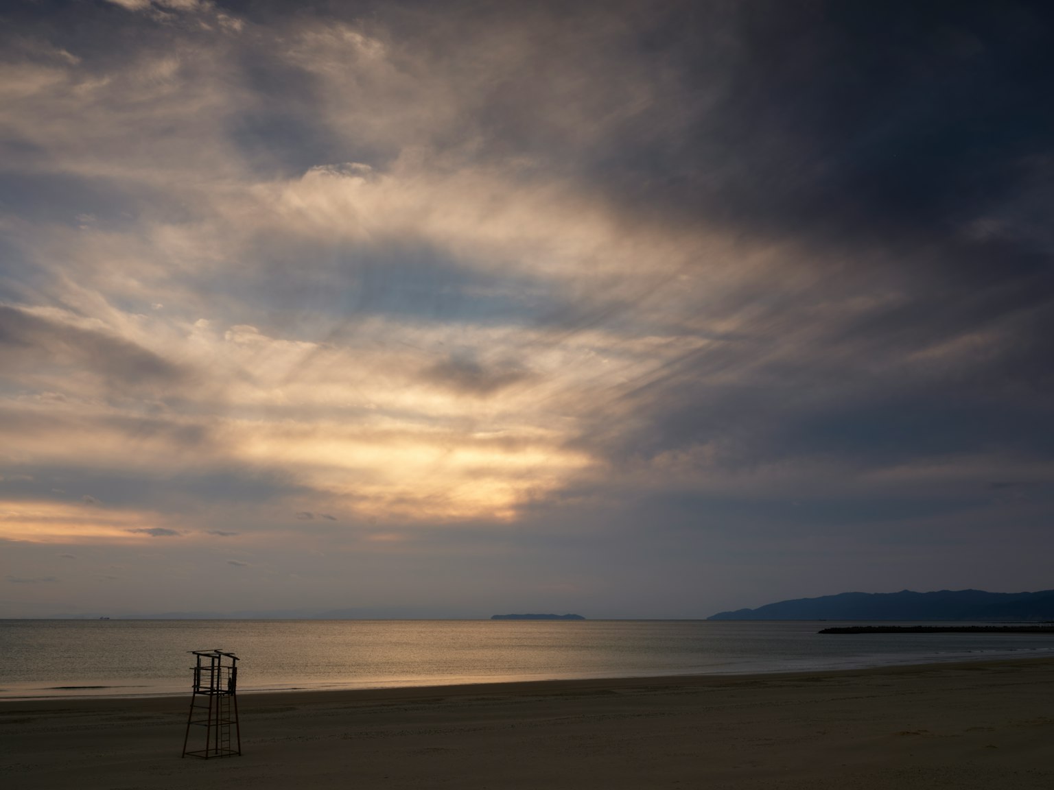 Côte calme avec des nuages sombres entourant un coucher de soleil sur la mer