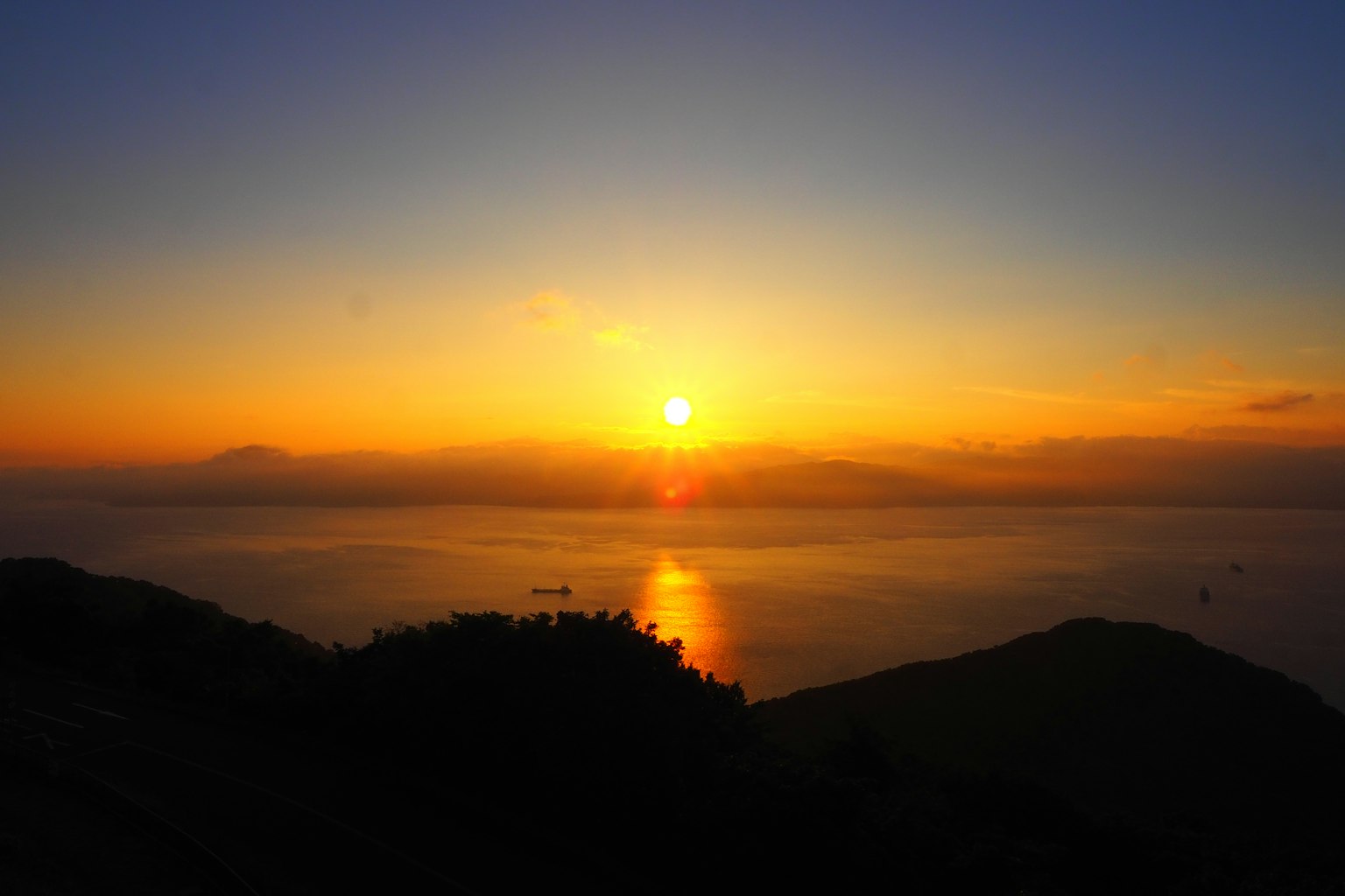 壮观的日落映照在海面上，轮廓分明的山丘