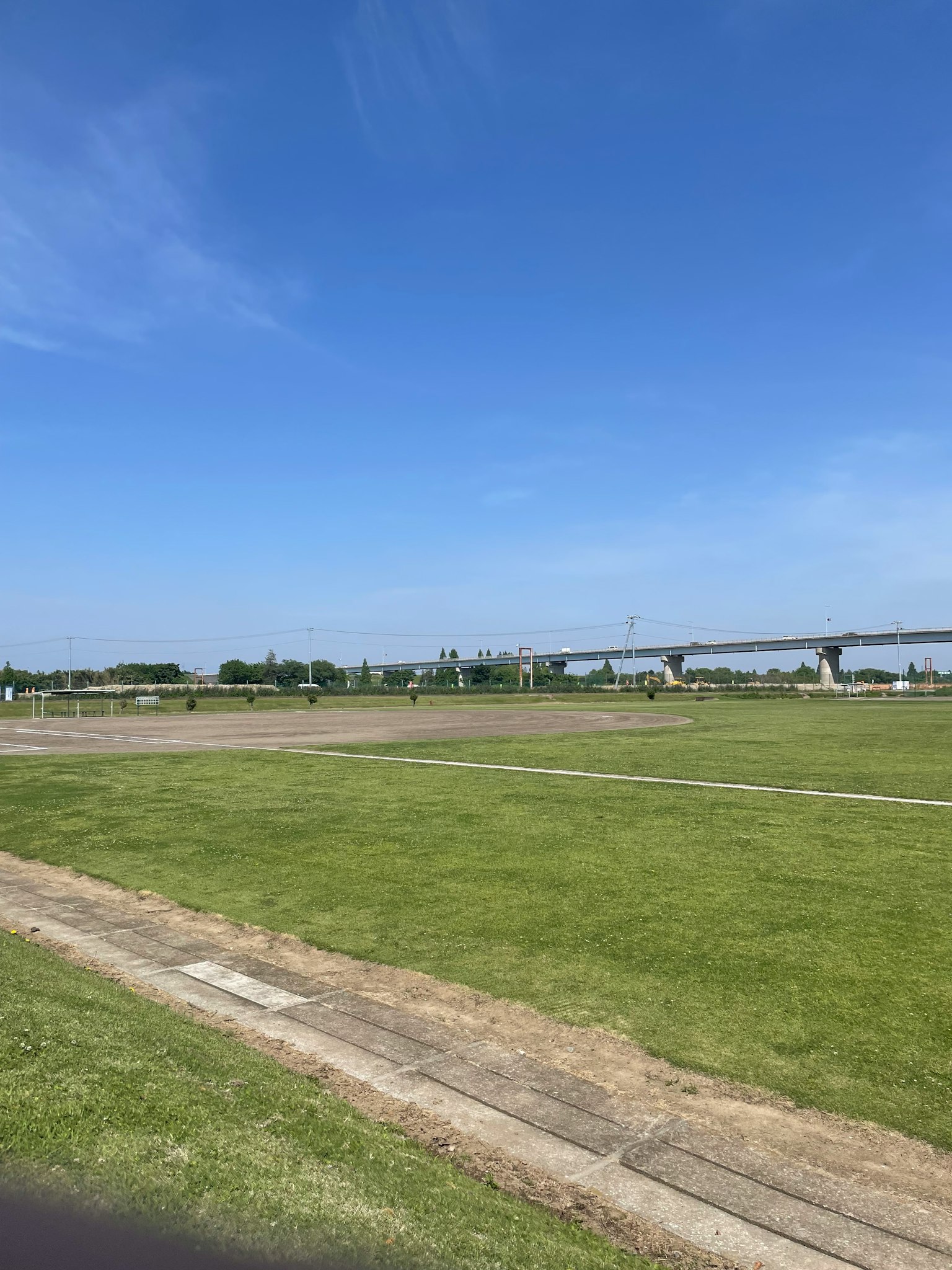 Pemandangan dengan langit biru dan rumput hijau jembatan terlihat di kejauhan