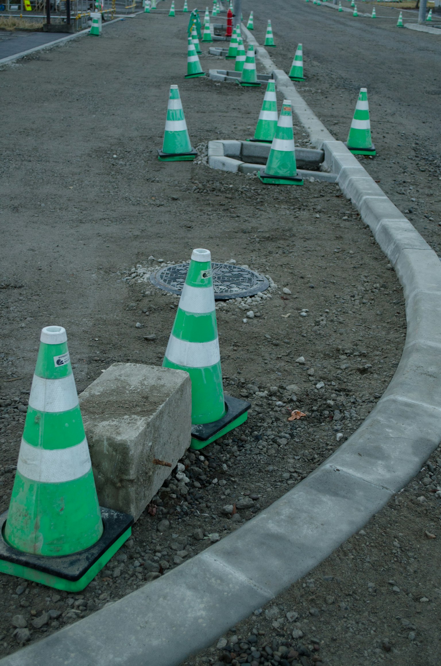 Bauplatz mit grünen und weißen Verkehrshütchen und gebogenem Betonbordstein