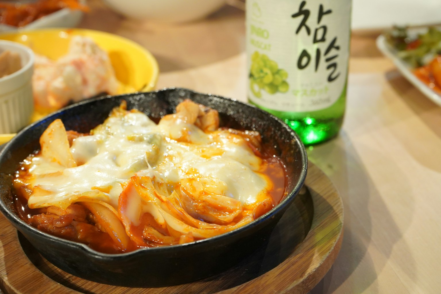 铁锅中盛着奶酪泡菜炖菜旁边有一瓶韩国饮料