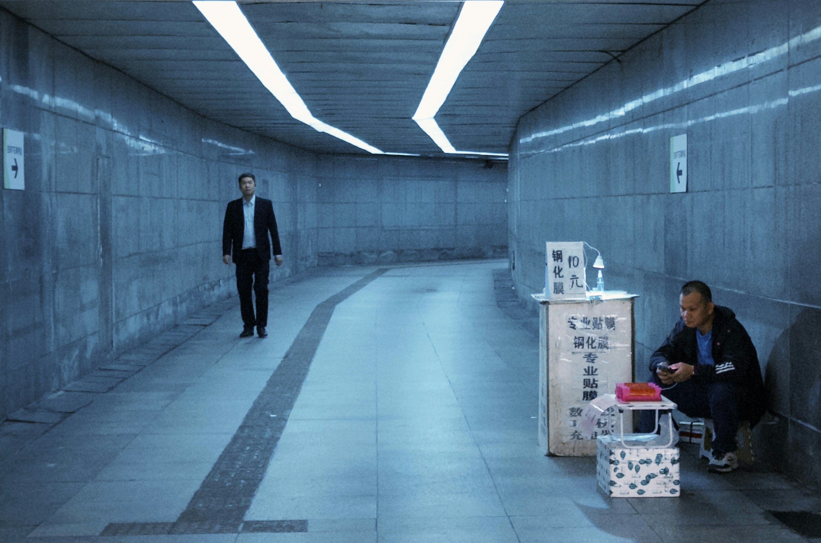 A suited man standing in a walled corridor beside a small table