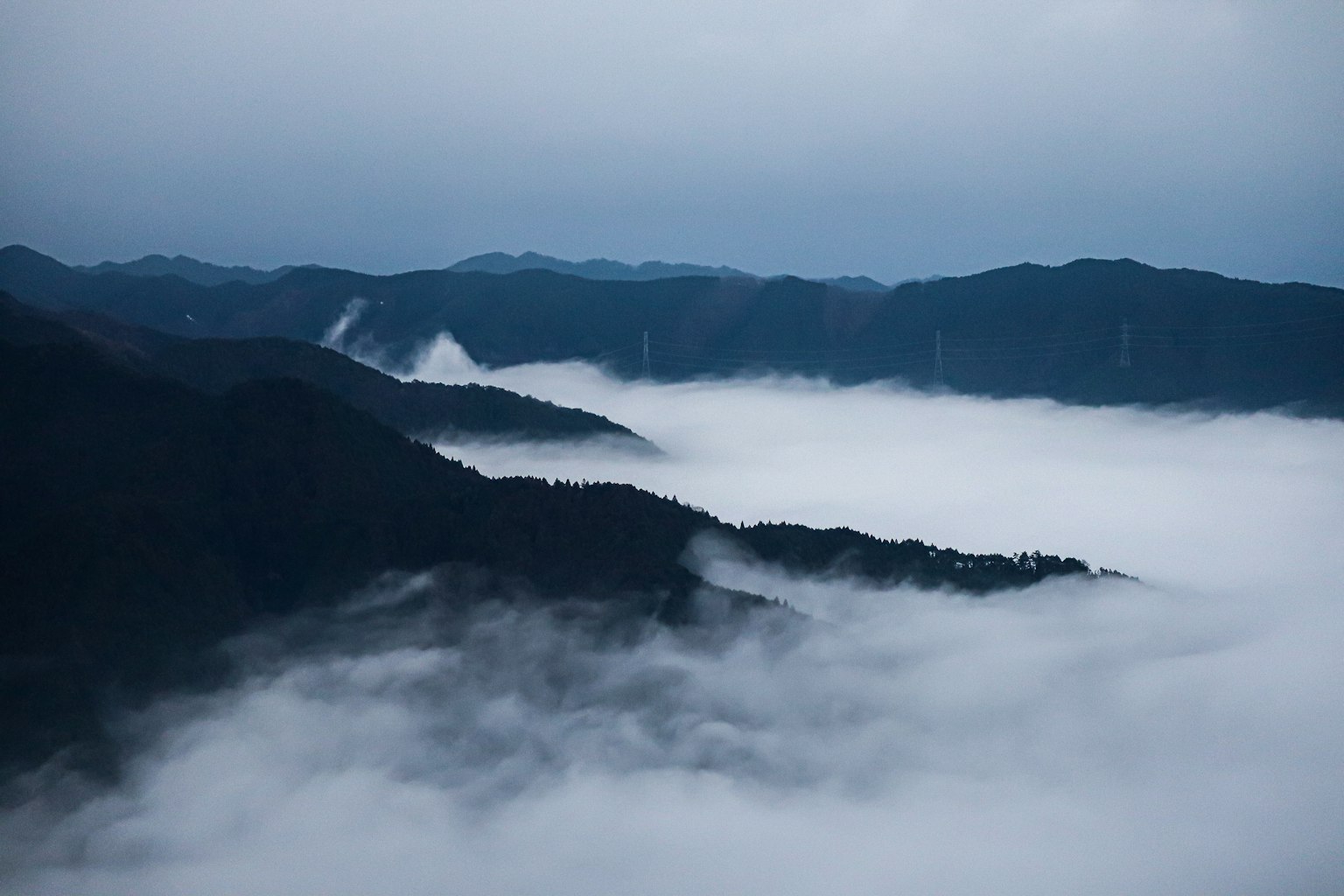 Pemandangan pegunungan yang tertutup kabut dengan langit biru tenang
