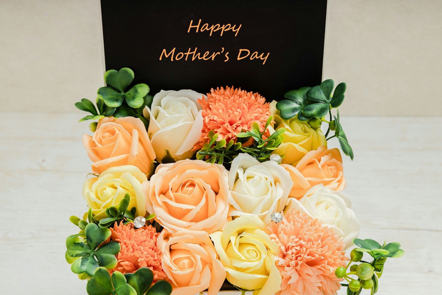 Arrangement floral avec des fleurs roses, oranges et blanches et une carte noire disant Joyeuse fête des mères