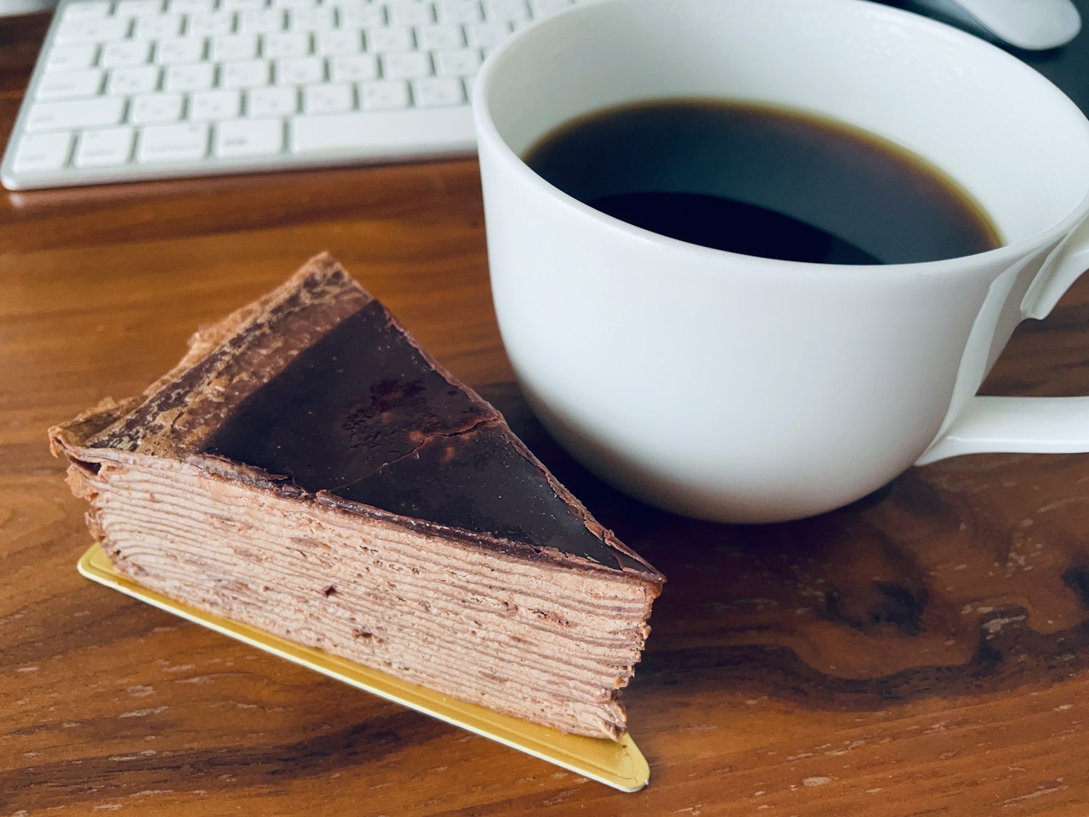 Una rebanada de pastel de chocolate junto a una taza de café negro sobre una mesa de madera