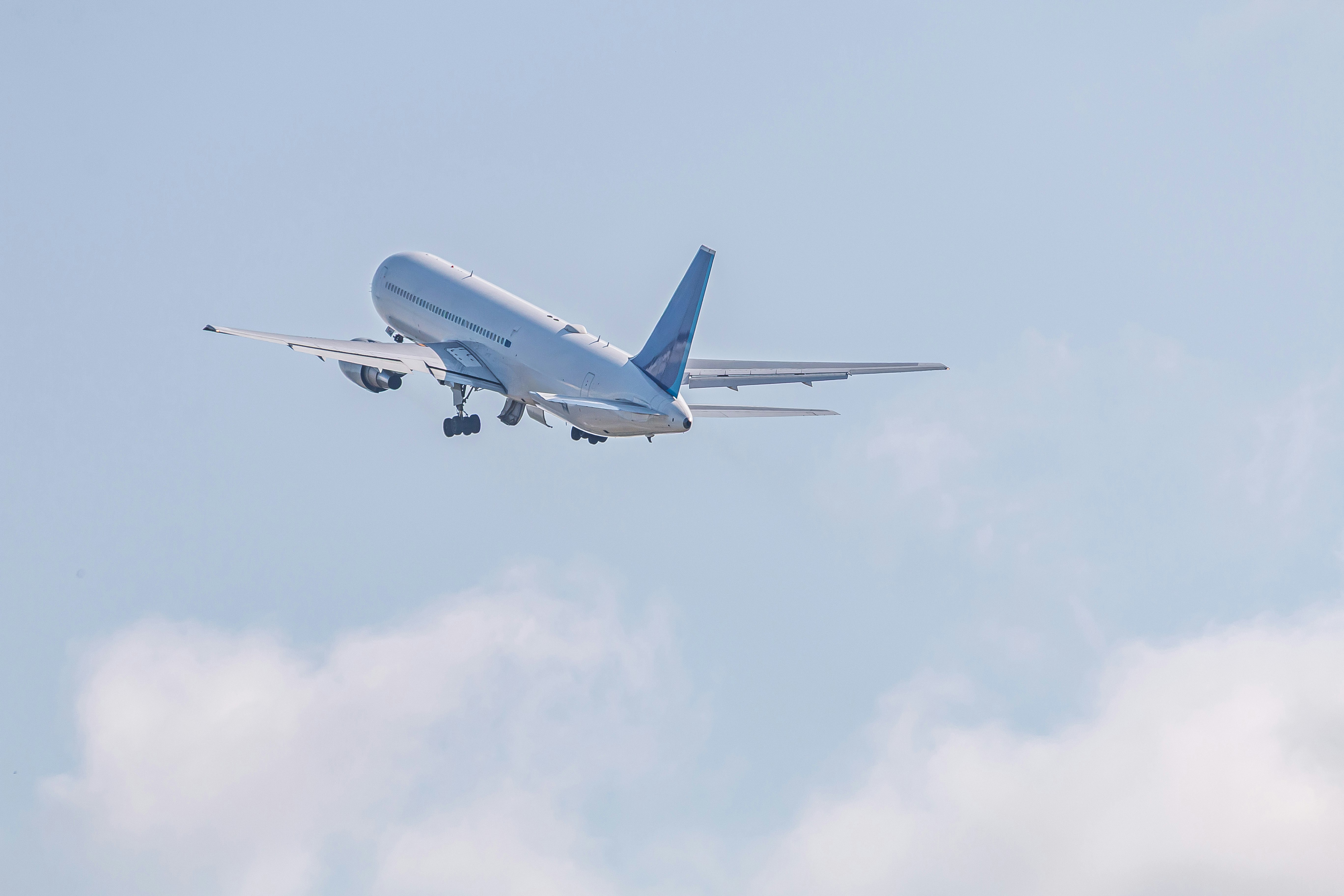 青空の下を飛ぶ旅客機の機首と翼