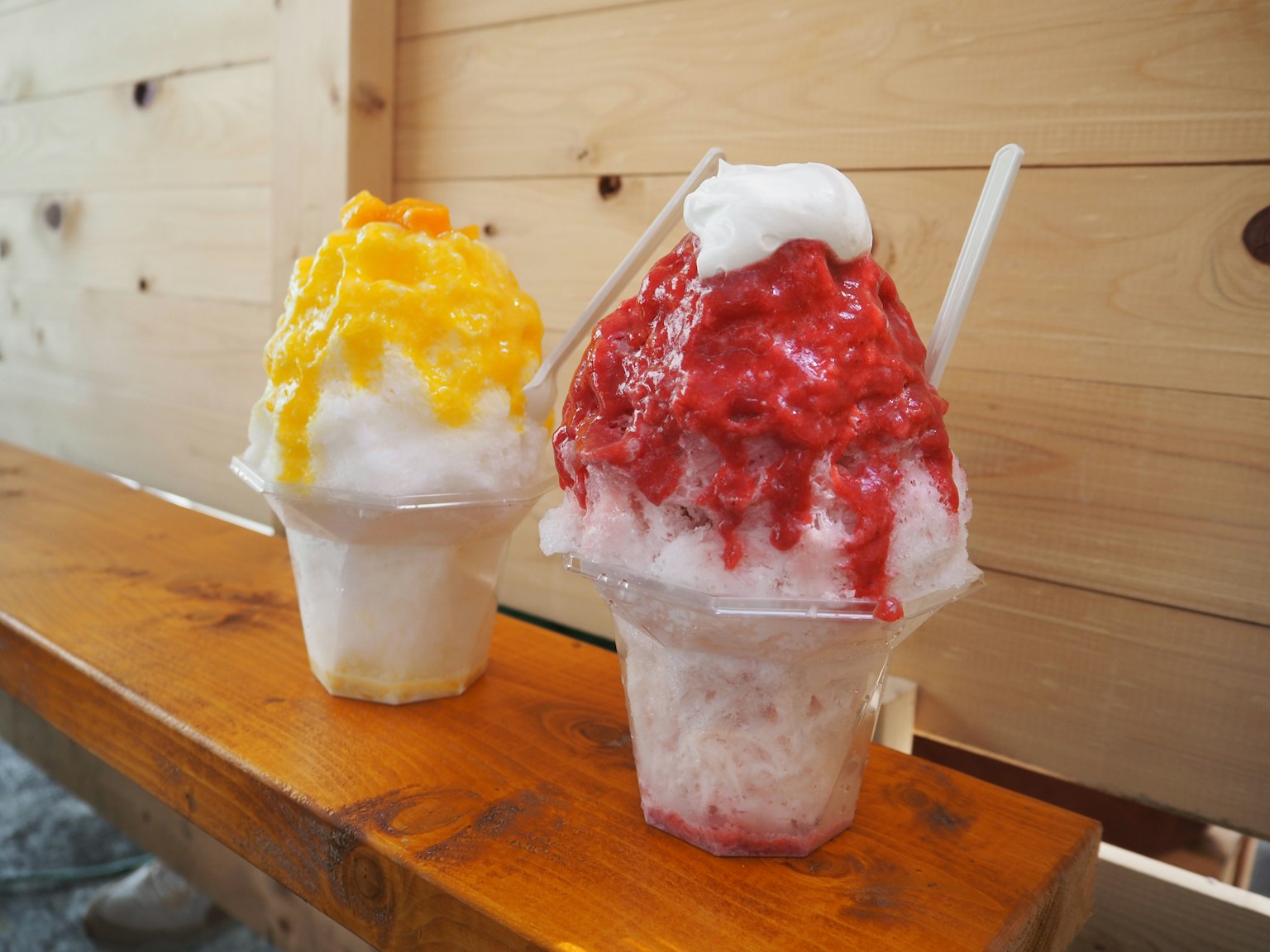 Two cups of shaved ice topped with yellow and red syrup