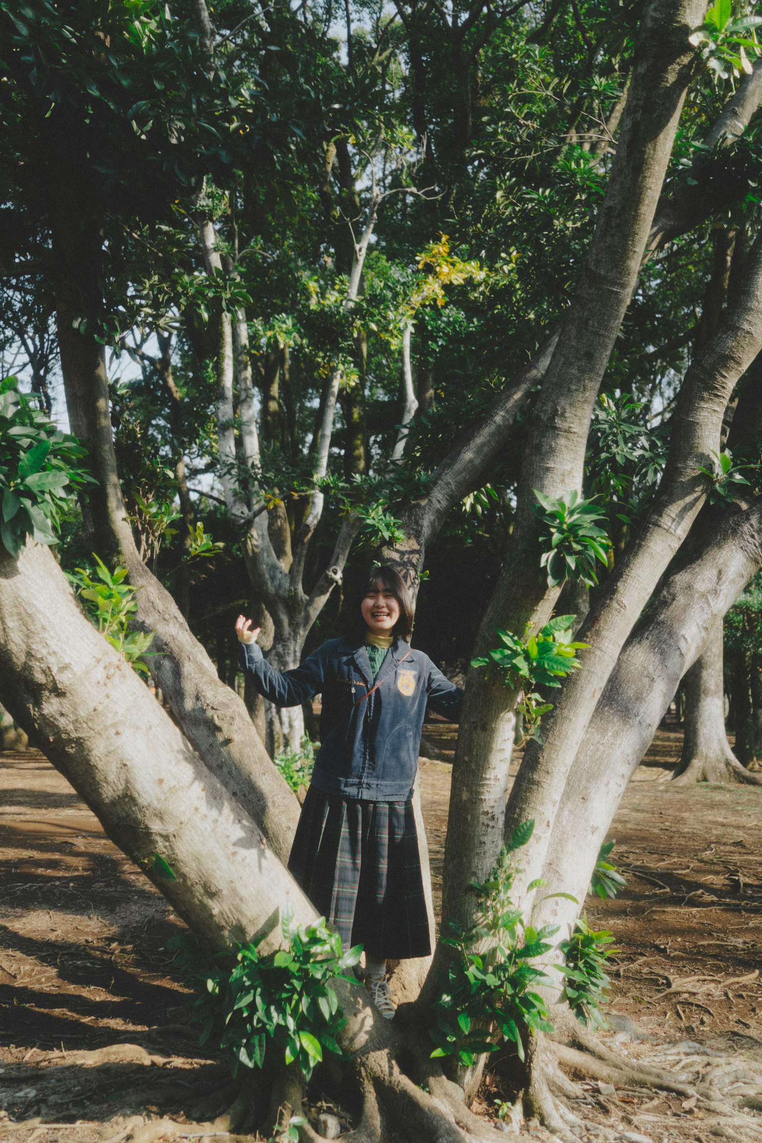 一名女性站在樹木之間，周圍環繞著綠色葉子，處於自然環境中