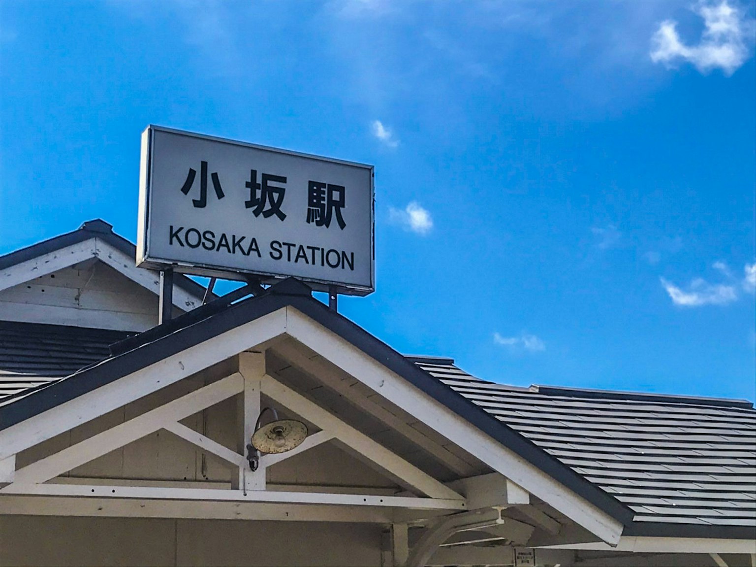 Papan nama Stasiun Kozaka dengan langit biru yang cerah