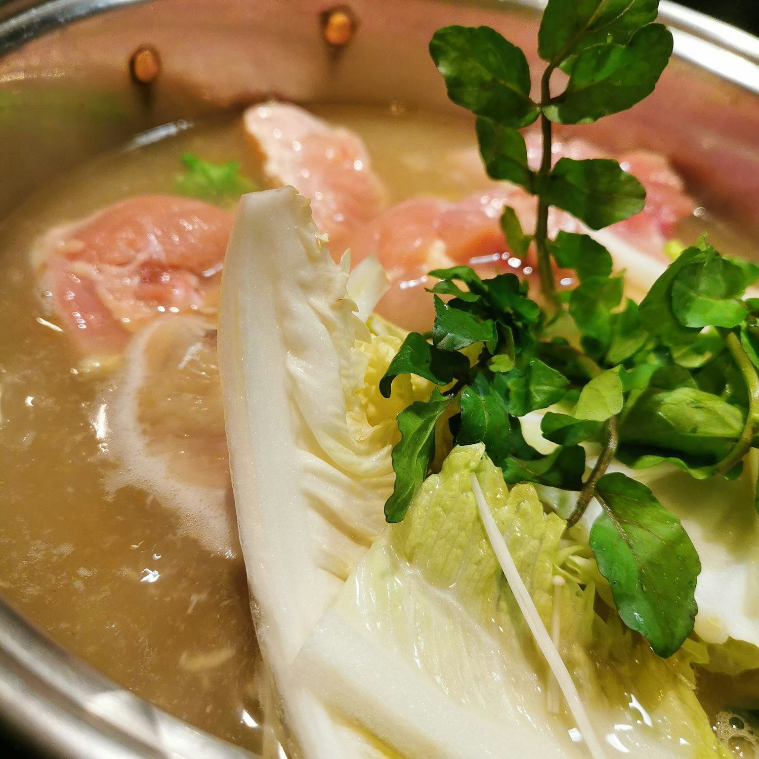 Close-up of a hot pot with sliced meat and fresh vegetables