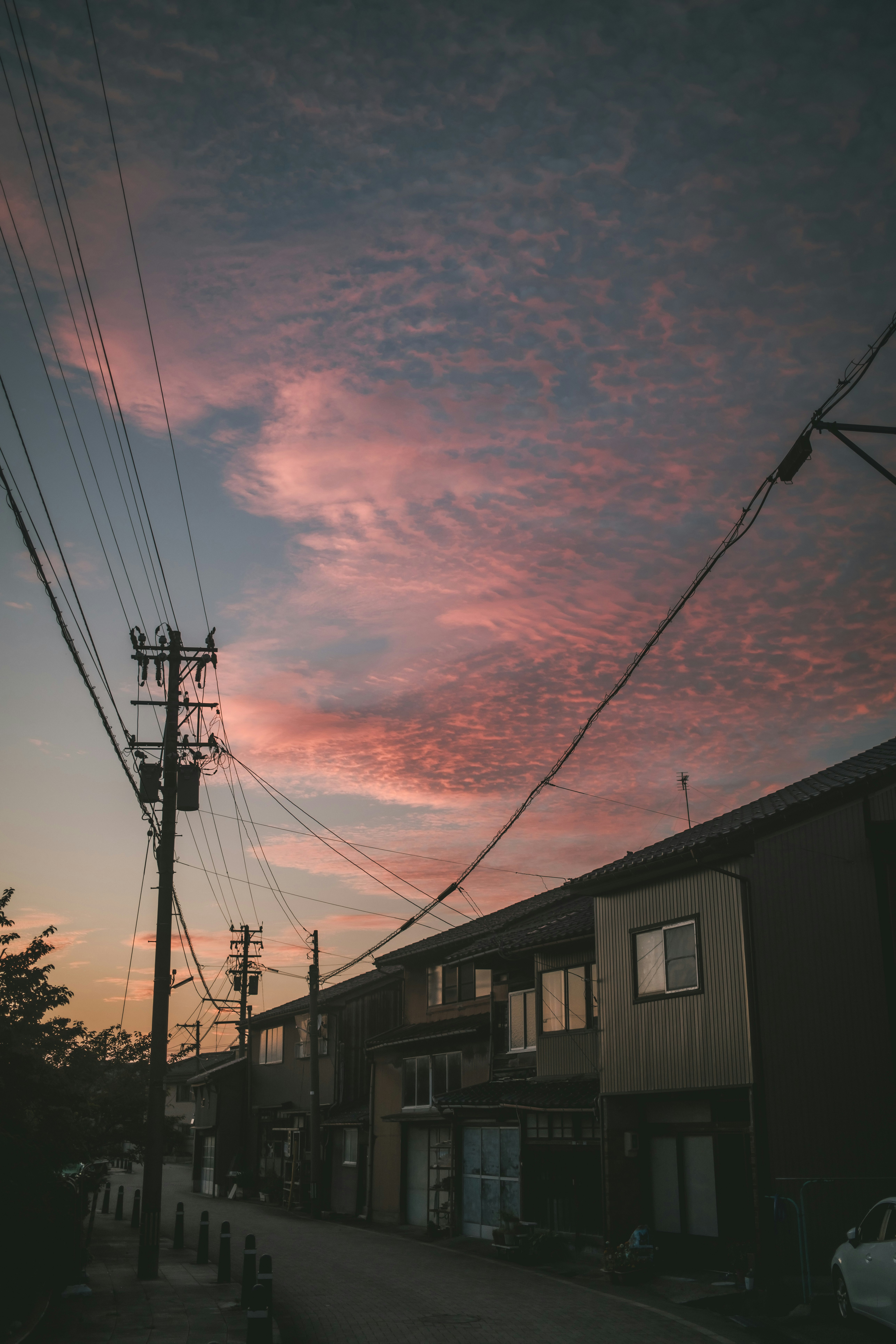 夕焼けの空と電線が走る路地の家並み