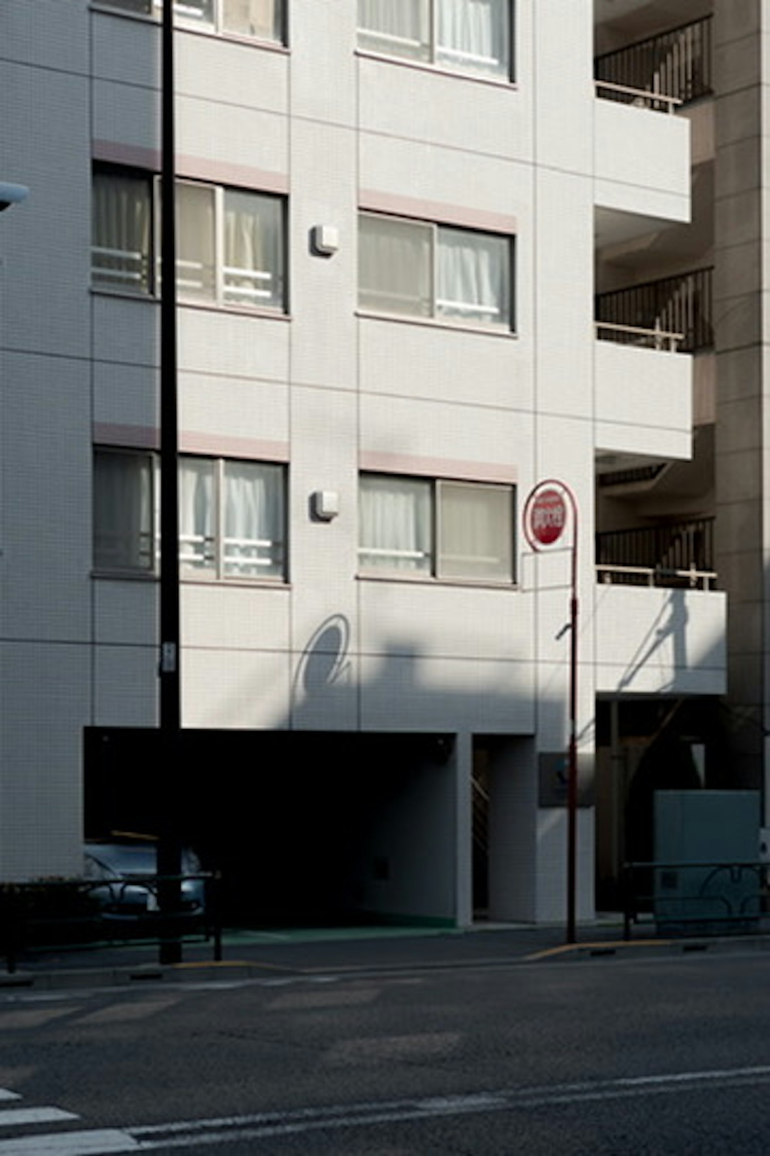 Vue de rue mettant en avant un bâtiment blanc avec des fenêtres visibles et un parking