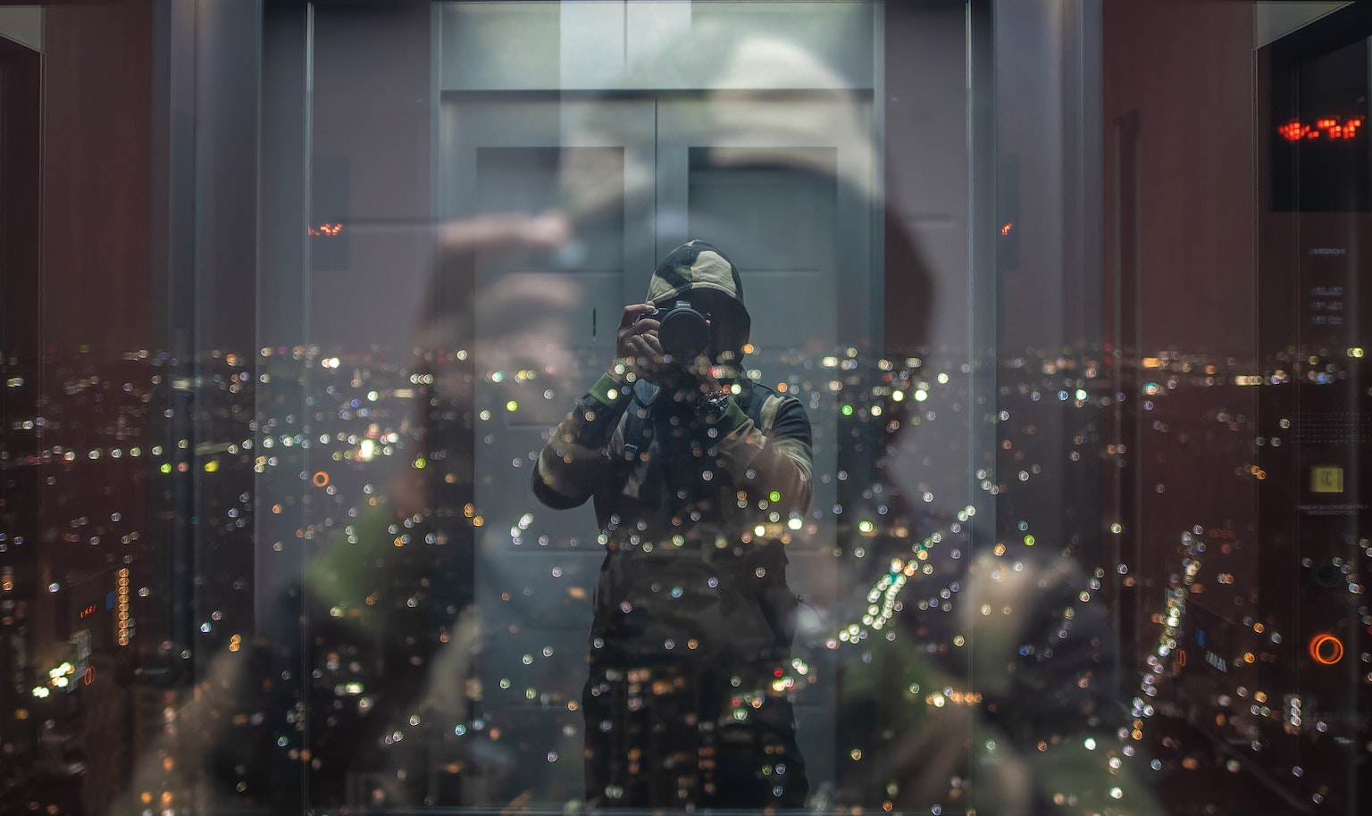 Autoritratto in un ascensore con riflesso del panorama urbano di notte
