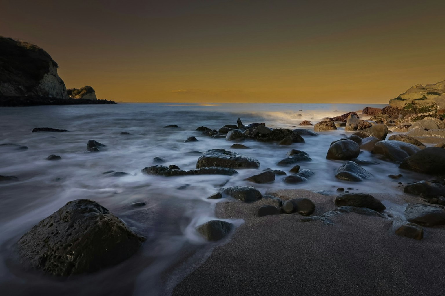 Escena costera con rocas y playa de arena por la noche Olas suaves acariciando las piedras