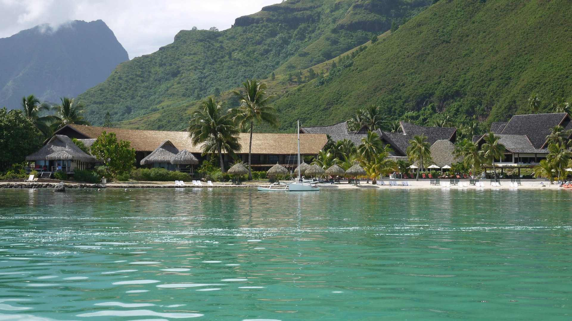 海邊度假村沿水面排列的度假小屋，遠處群山與青綠山丘