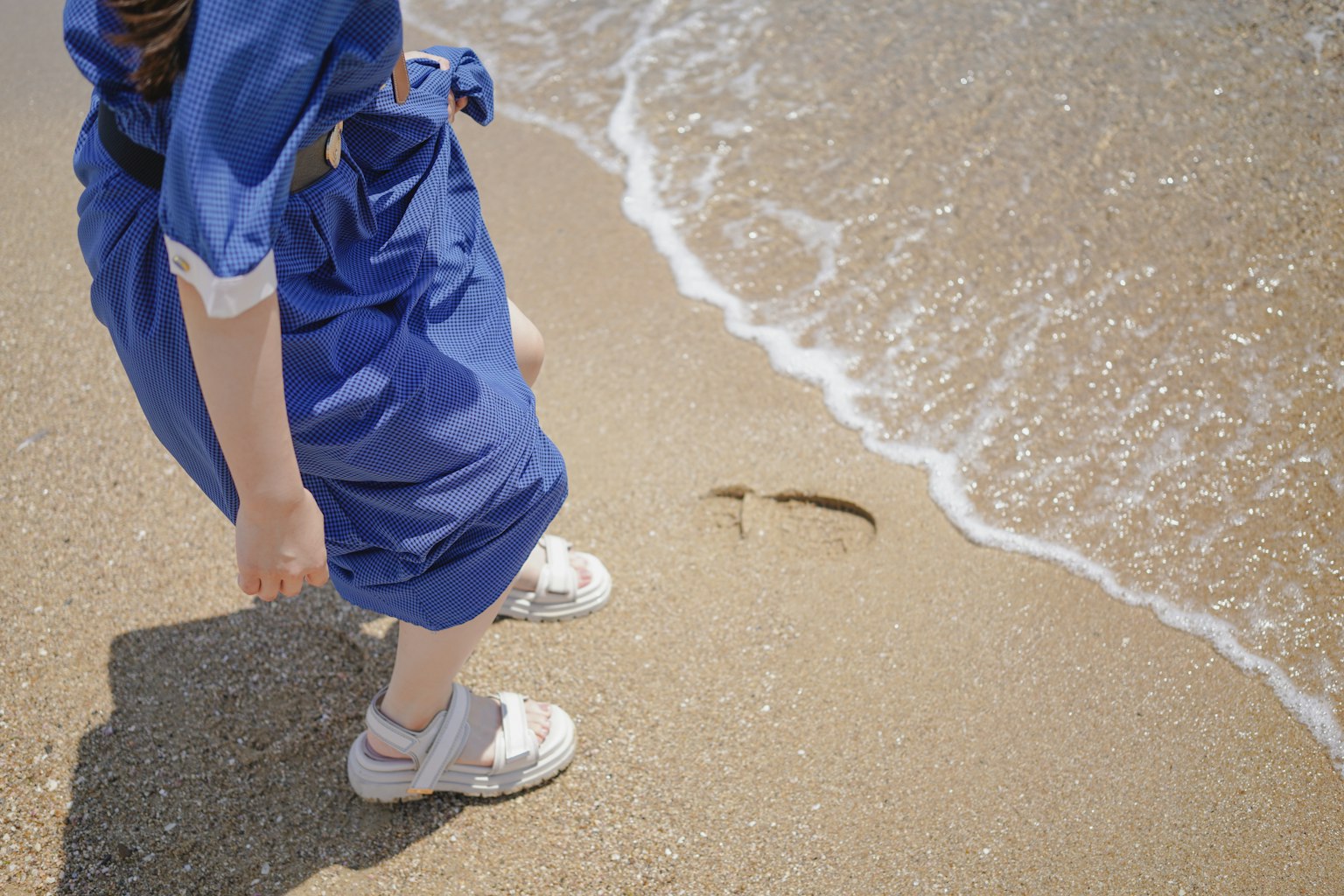 Anak berpakaian biru bermain di pantai dengan ombak