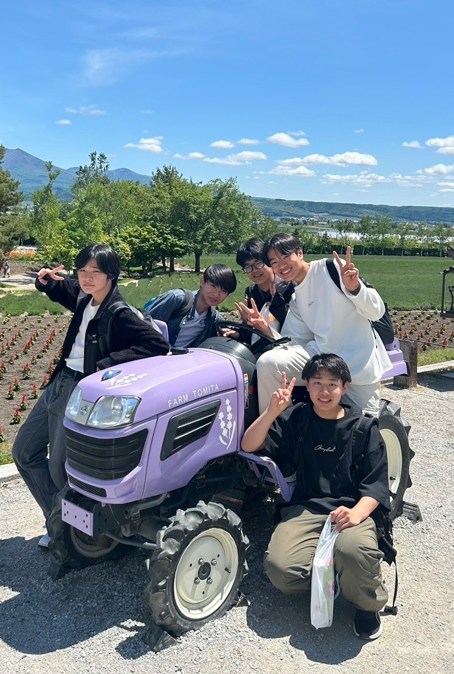 Group of young people sitting on a purple tractor blue sky and green landscape in the background
