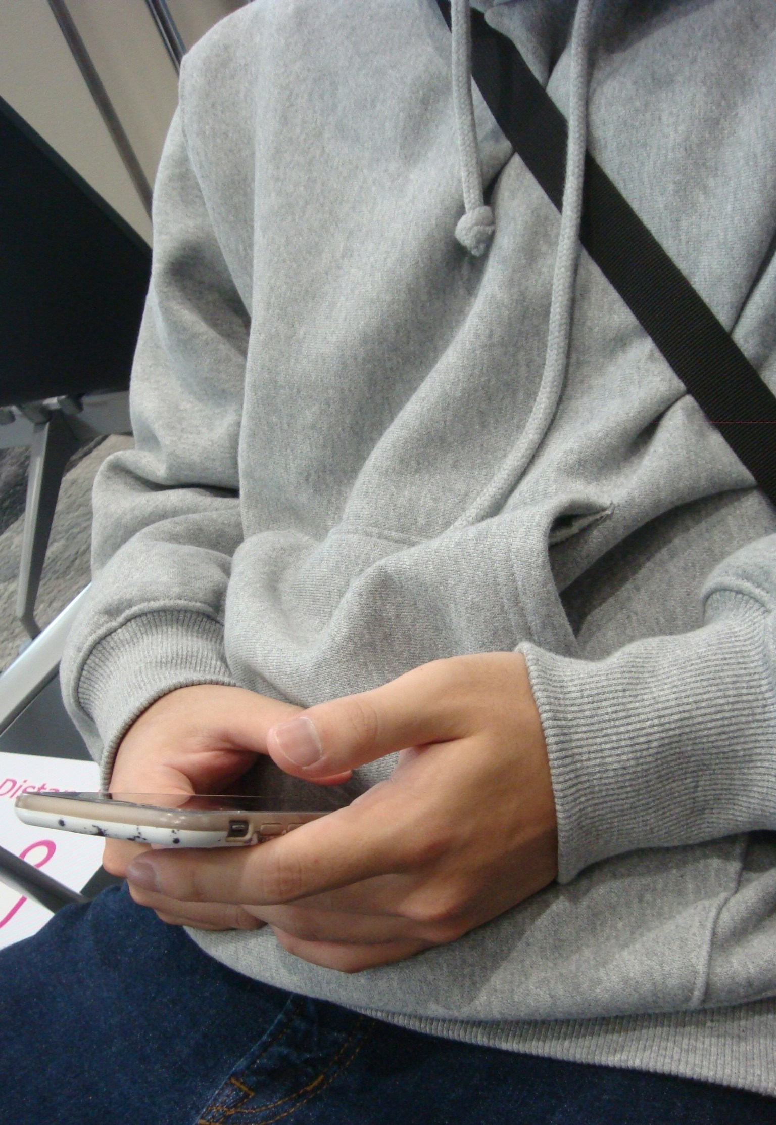 Close-up of hands using a smartphone while wearing a gray hoodie
