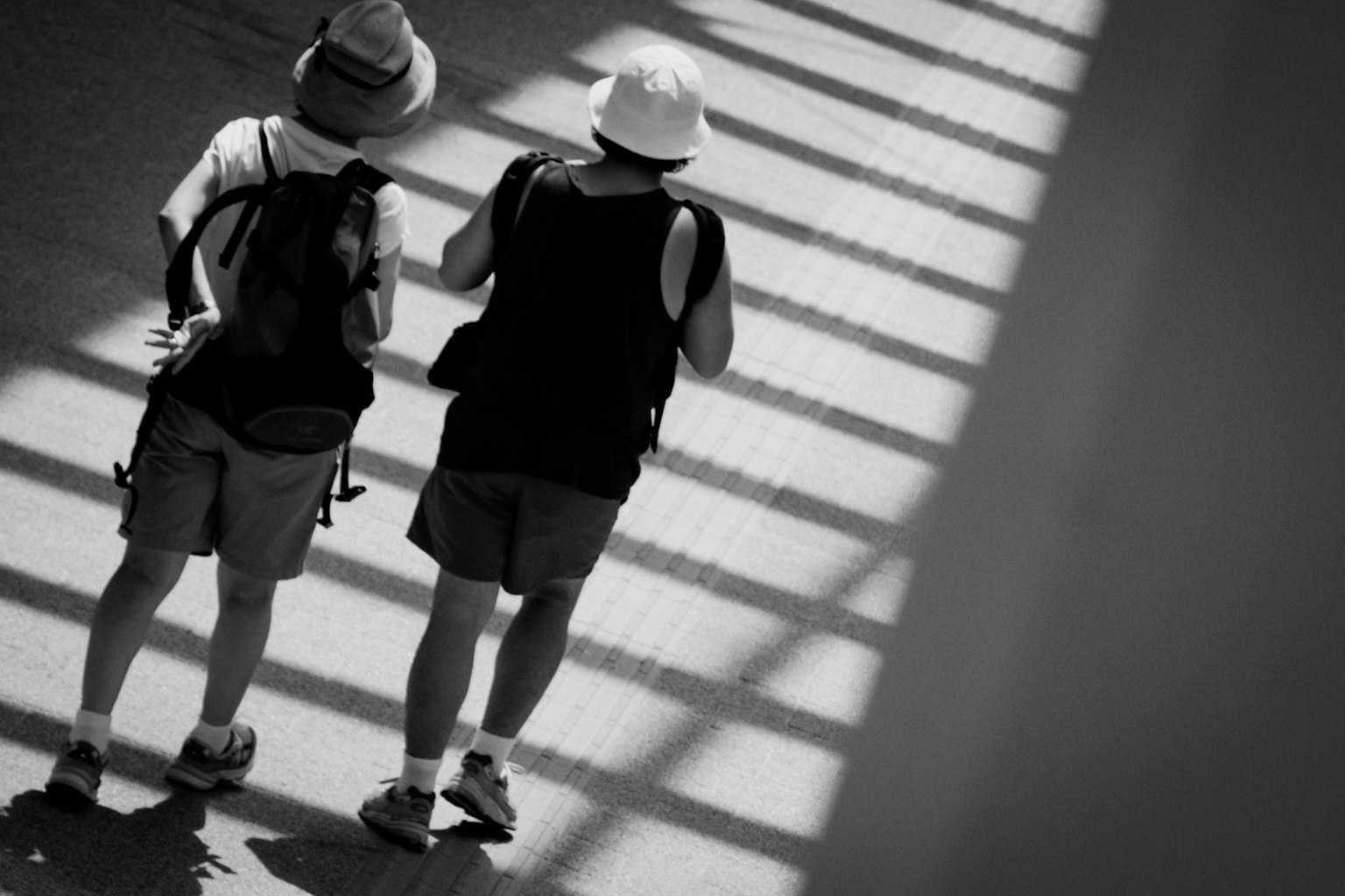 Two tourists wearing hats walking in shadow in black and white photo