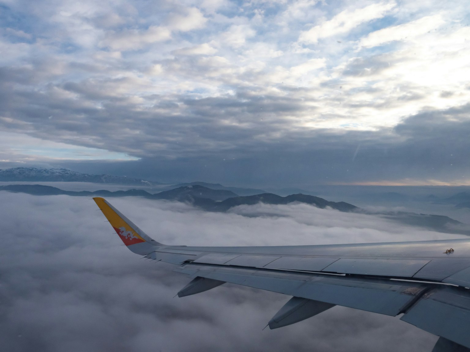 View of mountains above clouds with airplane wing