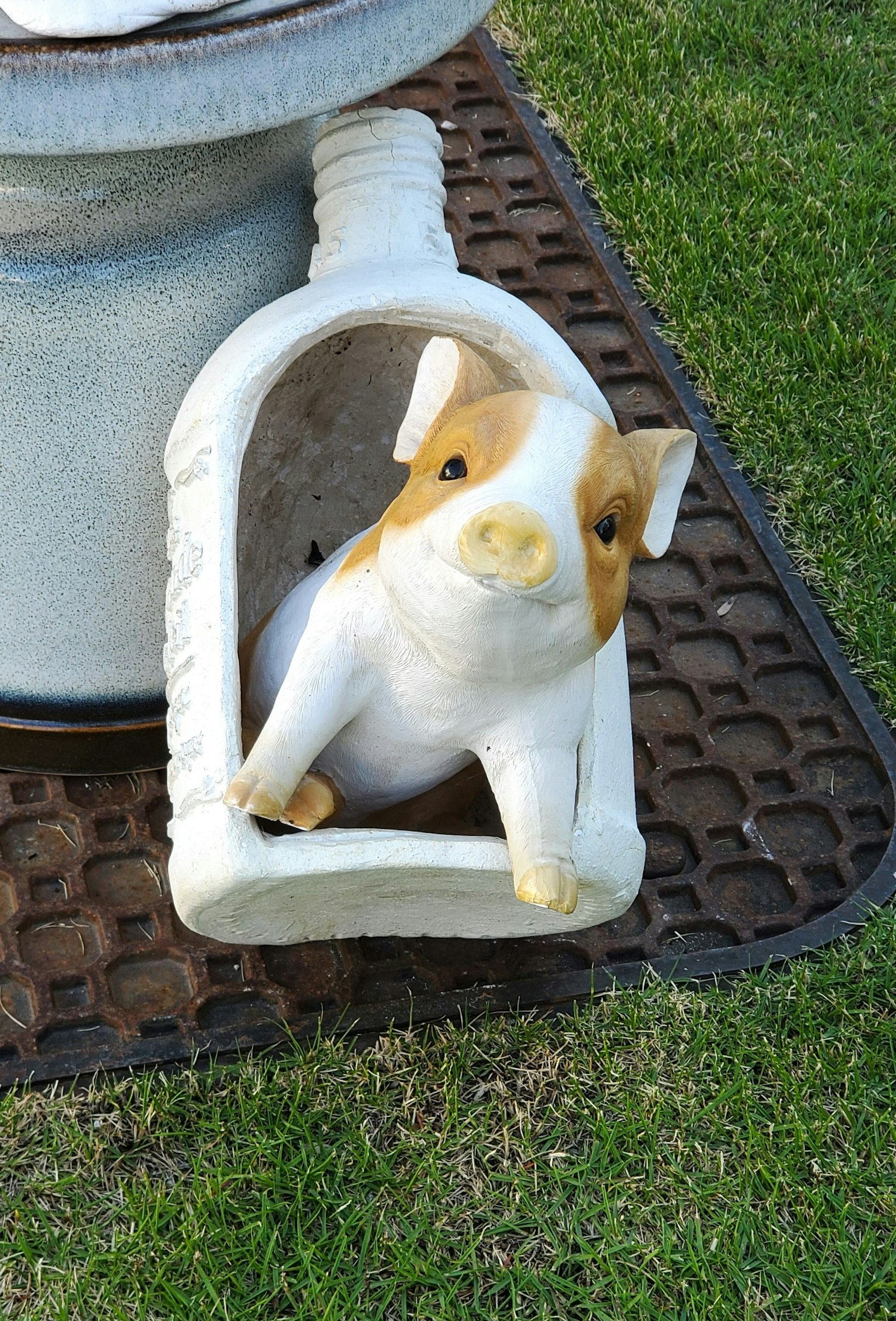 Una statuetta decorativa di maiale bianco e marrone poggiata sull'erba verde