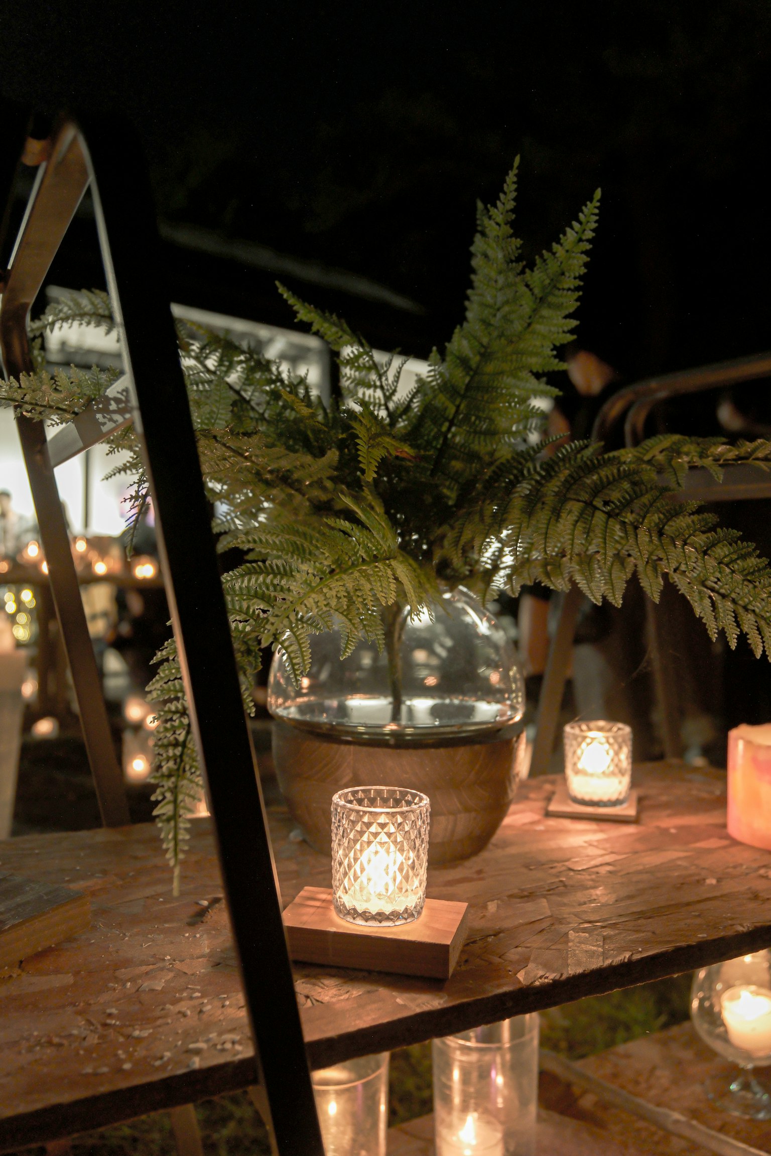 Mesa decorativa con un jarrón de vidrio con helechos y luz de velas por la noche