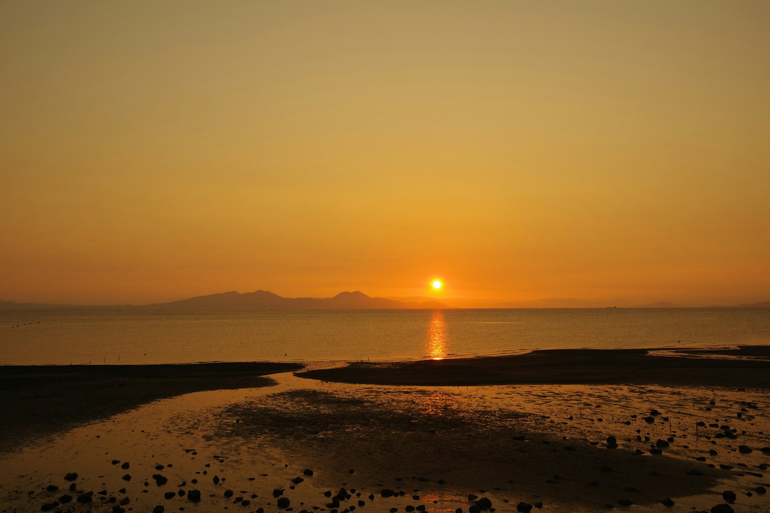 美丽的日落映照在海面上，岩石海岸和水流