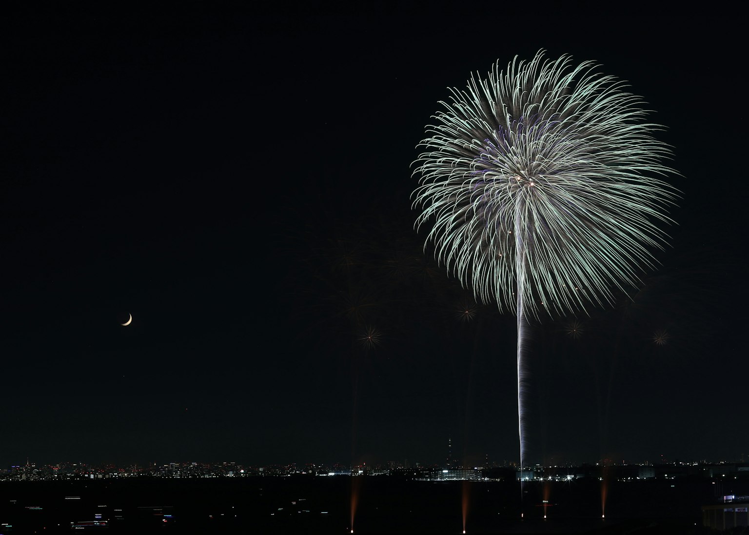 Großes Feuerwerk, das im Nachthimmel mit Stadtlichtern im Hintergrund explodiert