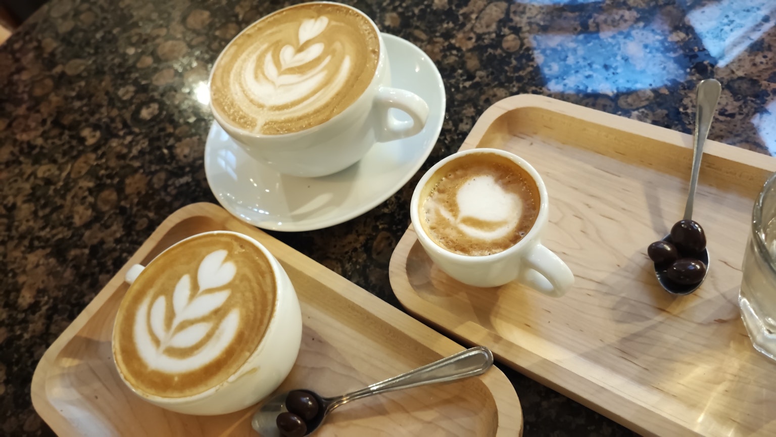 ถ้วยกาแฟสามใบที่มีศิลปะลาเต้บนถาดไม้