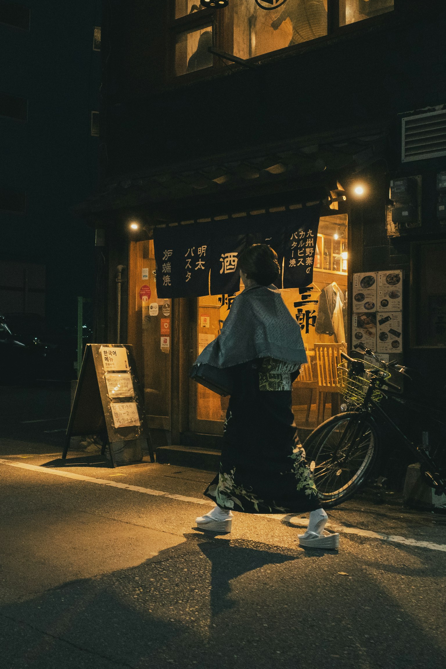 一位穿著傳統服裝的女性在夜晚走過一家日式商店