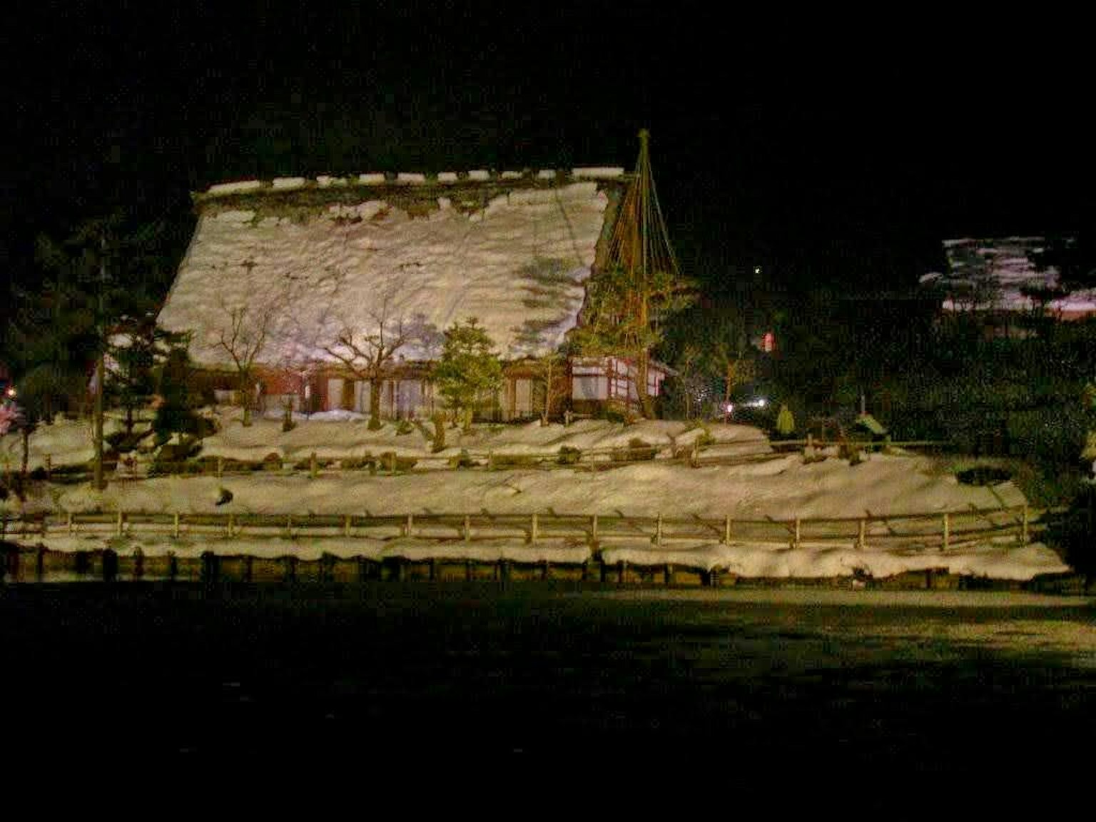 บ้านญี่ปุ่นแบบดั้งเดิมที่ปกคลุมด้วยหิมะในตอนกลางคืนพร้อมภูมิทัศน์รอบๆ