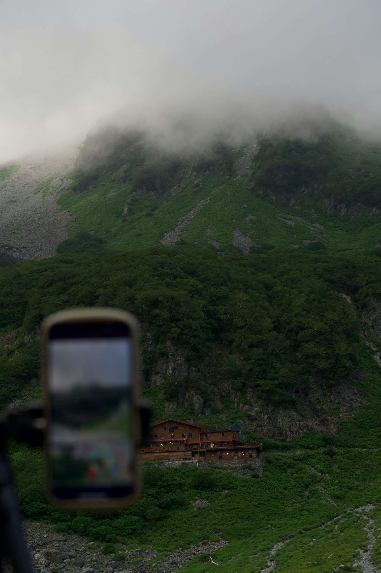 Mountain shrouded in mist with lush greenery and a smartphone in the foreground